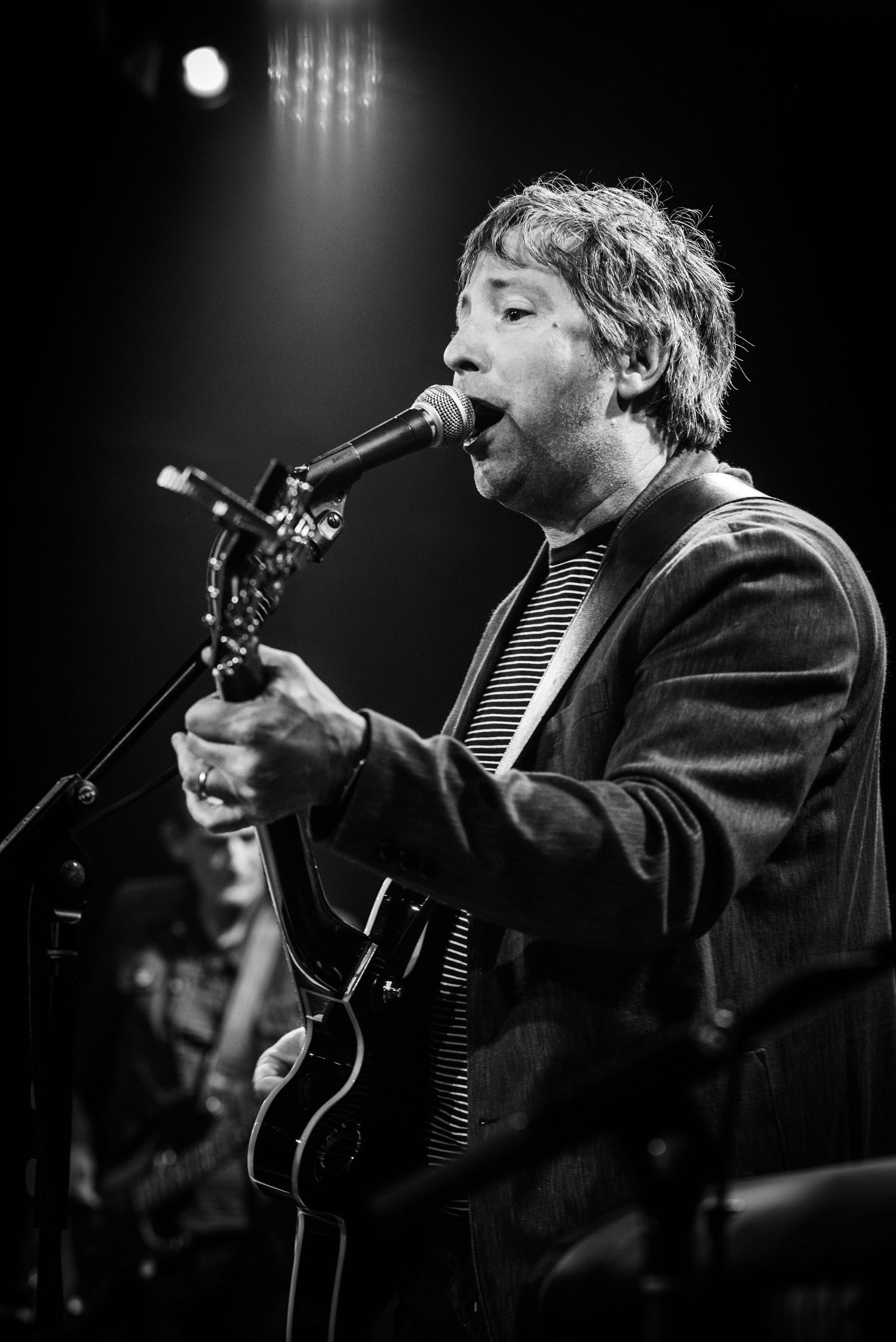 Black and white shot of performer singing and playing guitar on stage under spotlight.