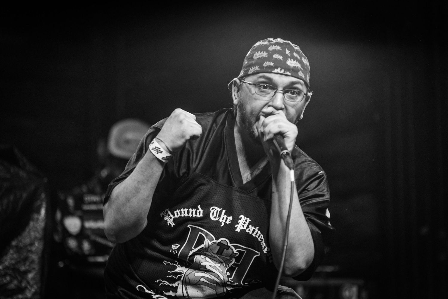 Close-up black and white concert photo of performer in bandana gripping microphone.