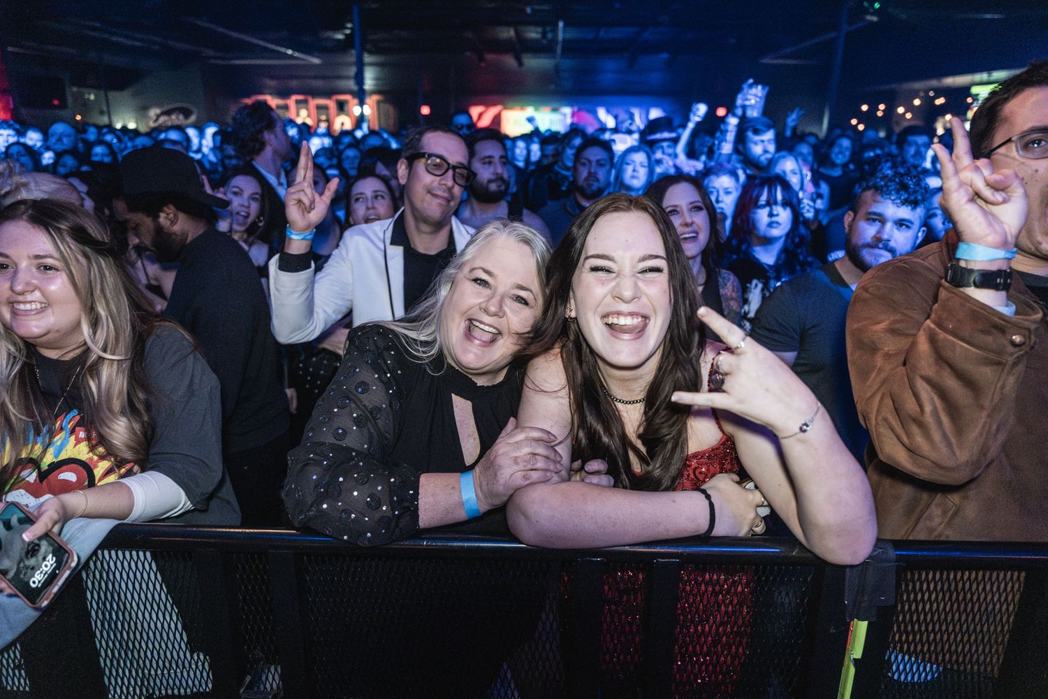 Concert audience members smiling and enjoying live performance at music venue.