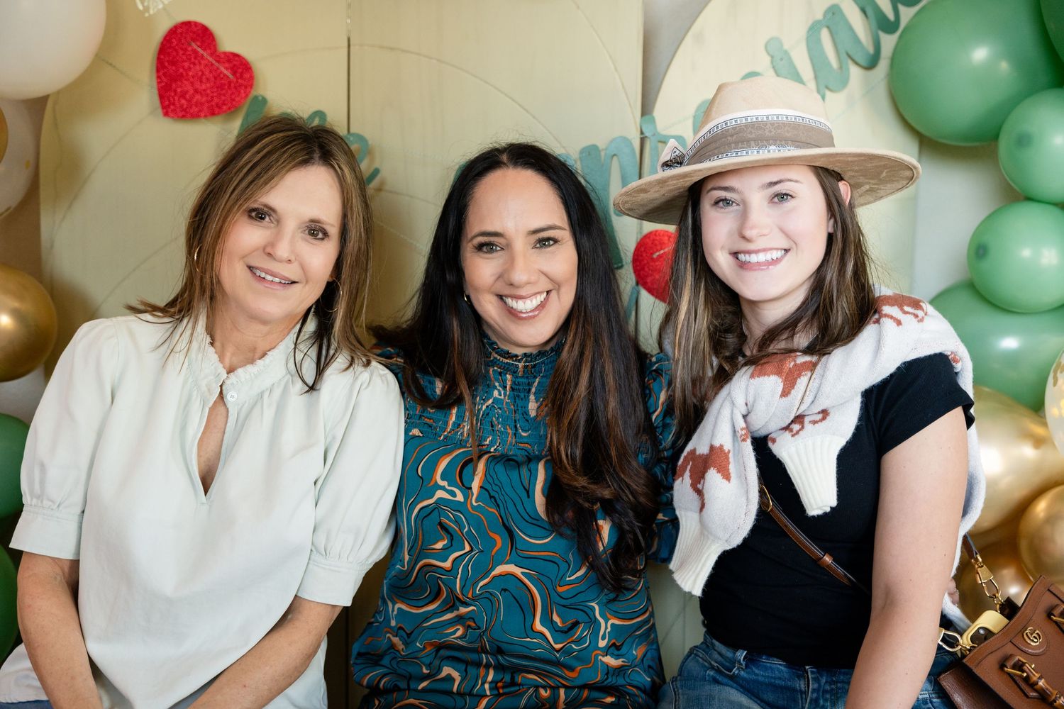 Three people posing at a party with balloon decorations in the background.