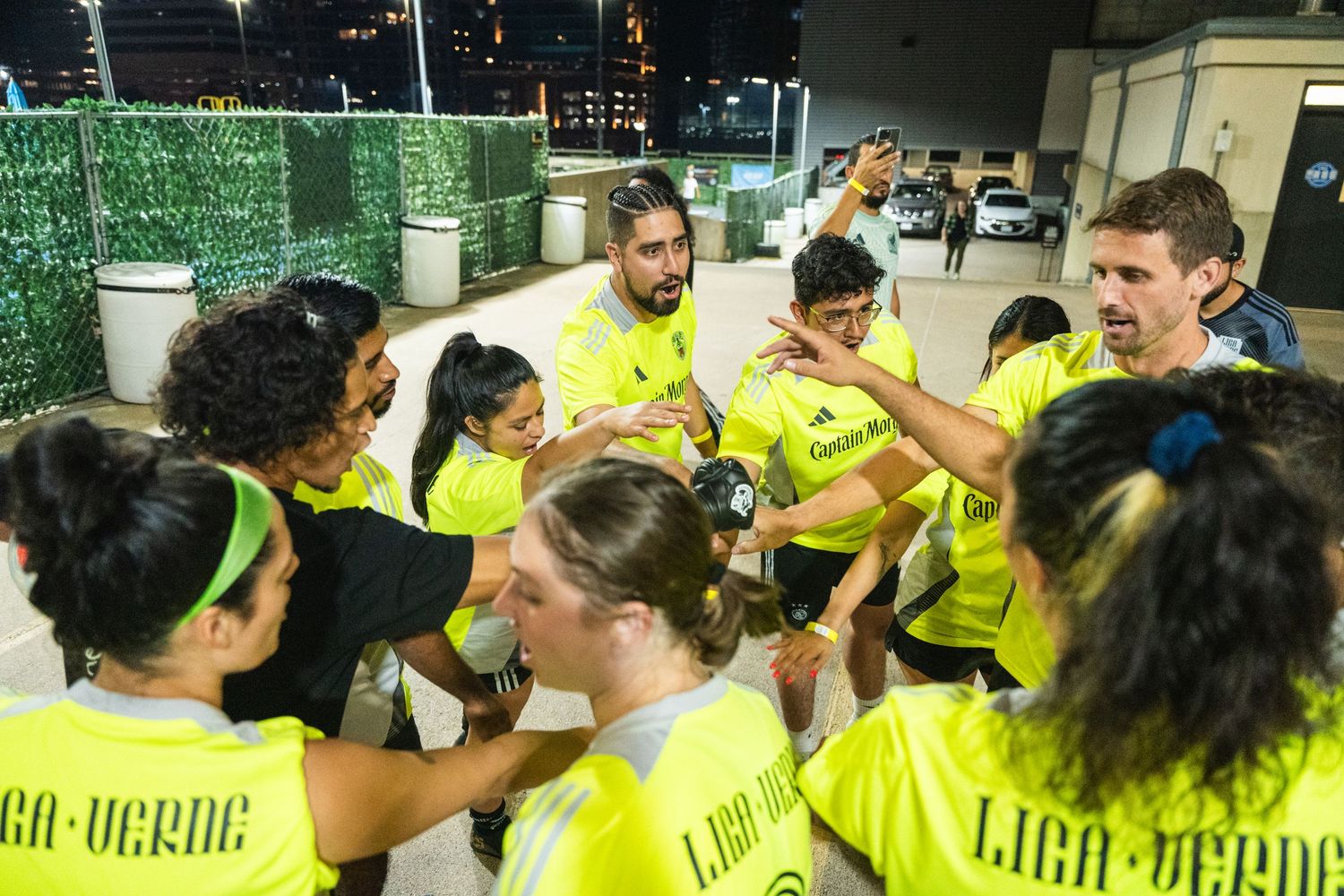 Team members in fluorescent yellow jerseys join hands in a pre-game huddle.