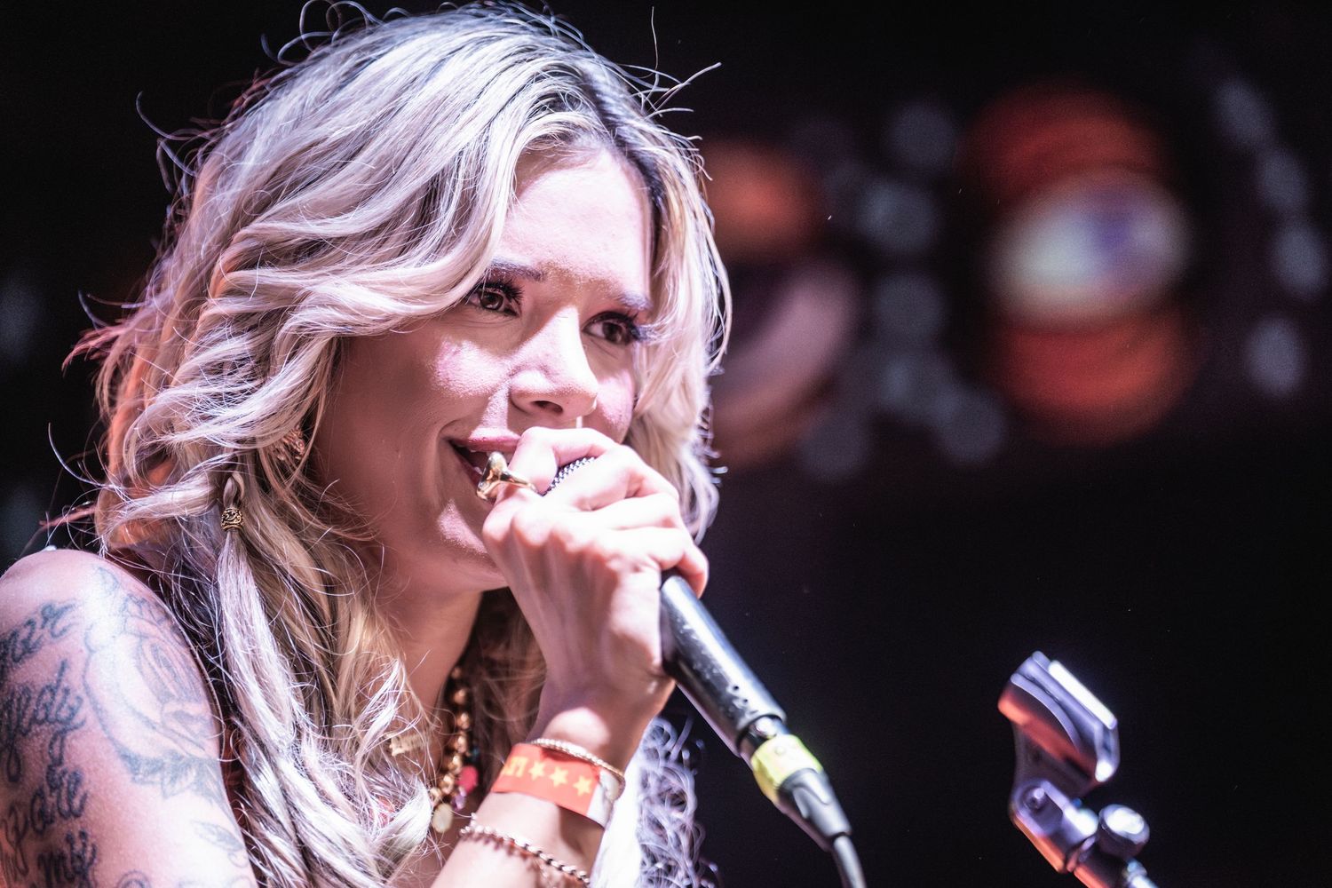 A woman in denim jacket and blonde hair performs passionately on stage with a microphone.