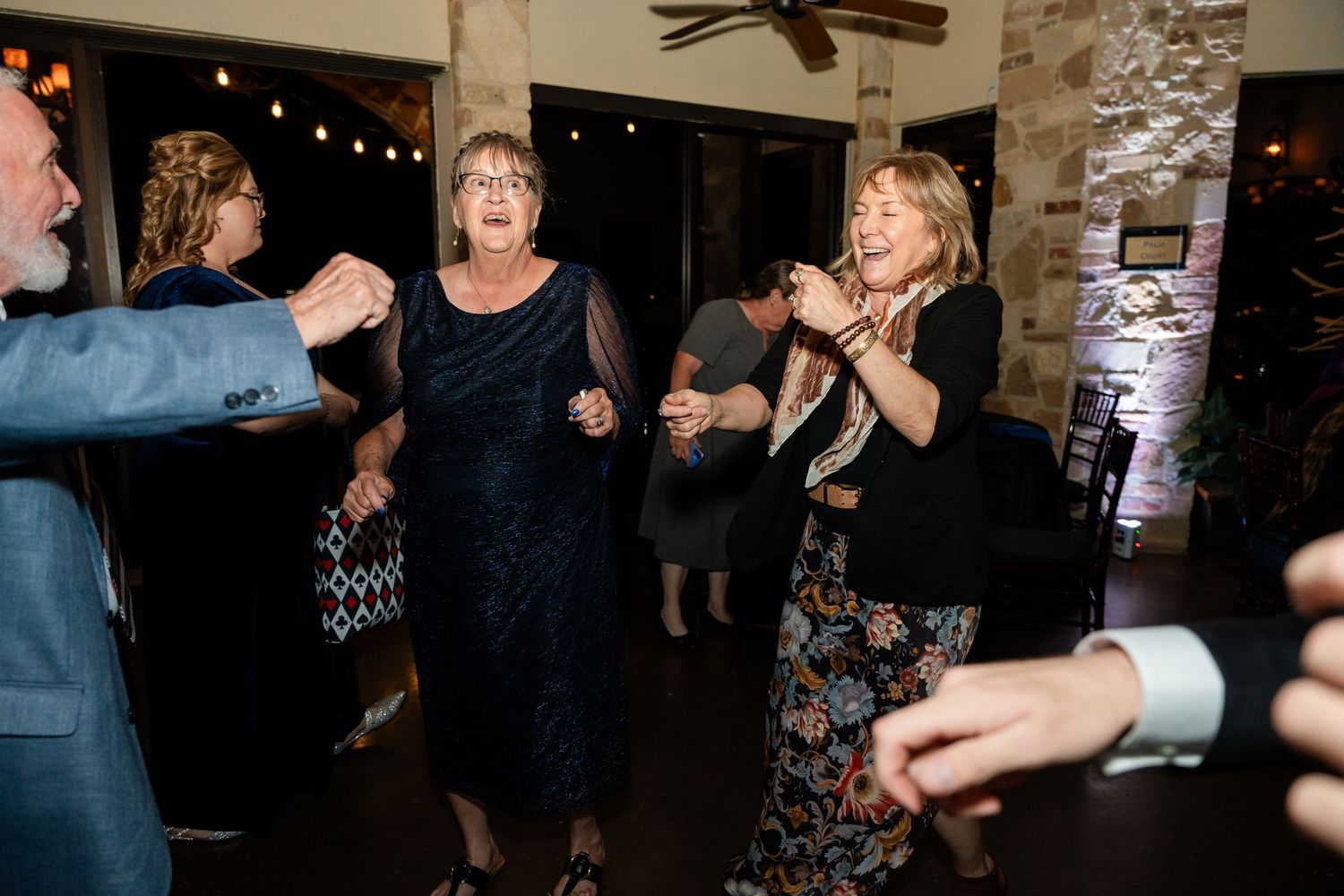 Guests dancing enthusiastically at a wedding reception with decorative lighting on stone walls.