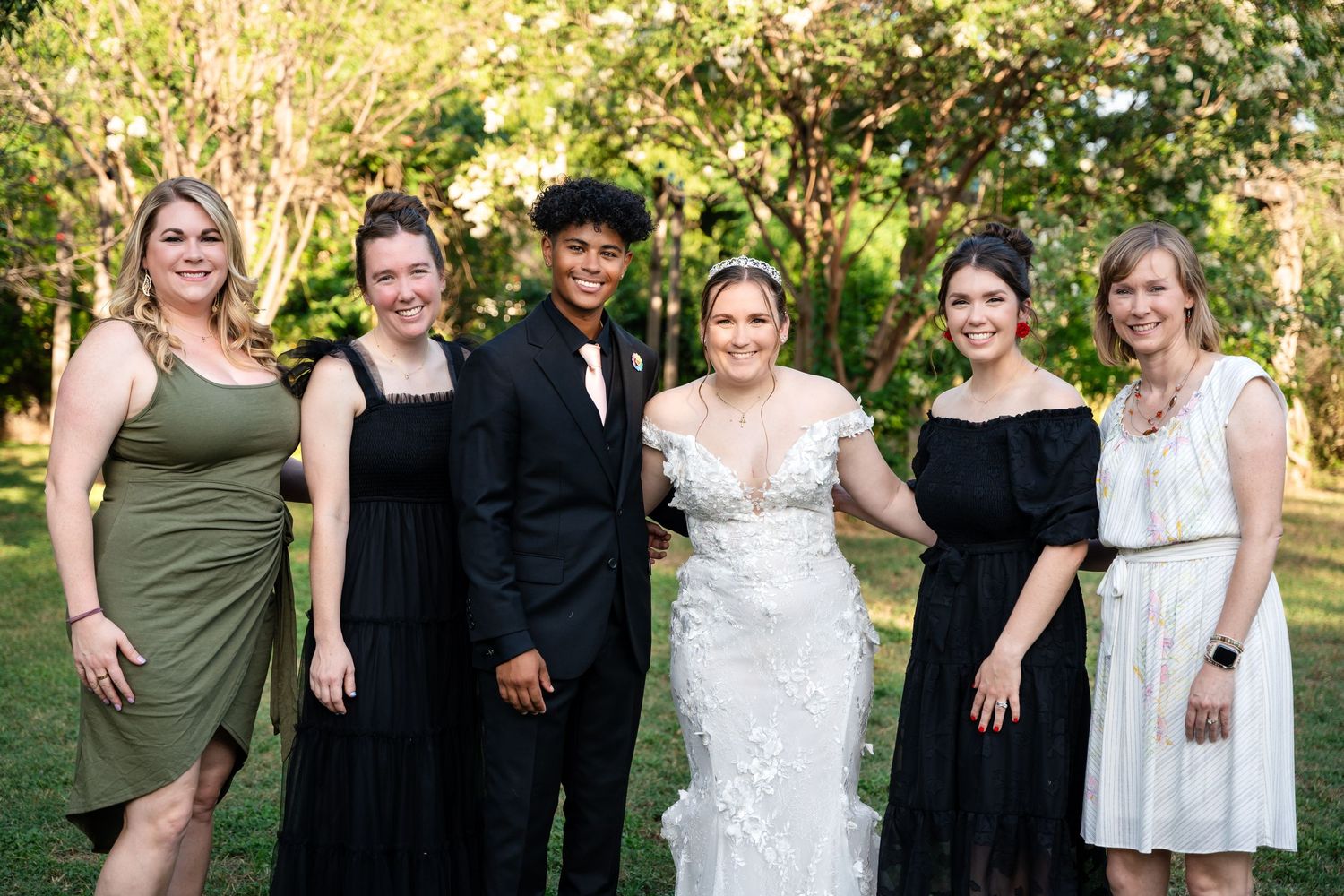 Wedding party members pose together outdoors in mix of formal attire.