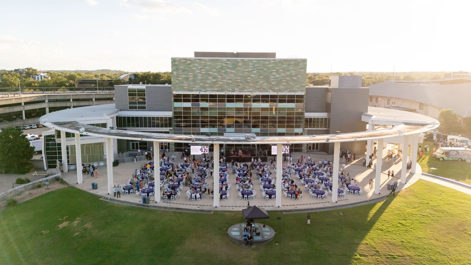 Aerial view of modern amphitheater filled with crowd during sunset event.