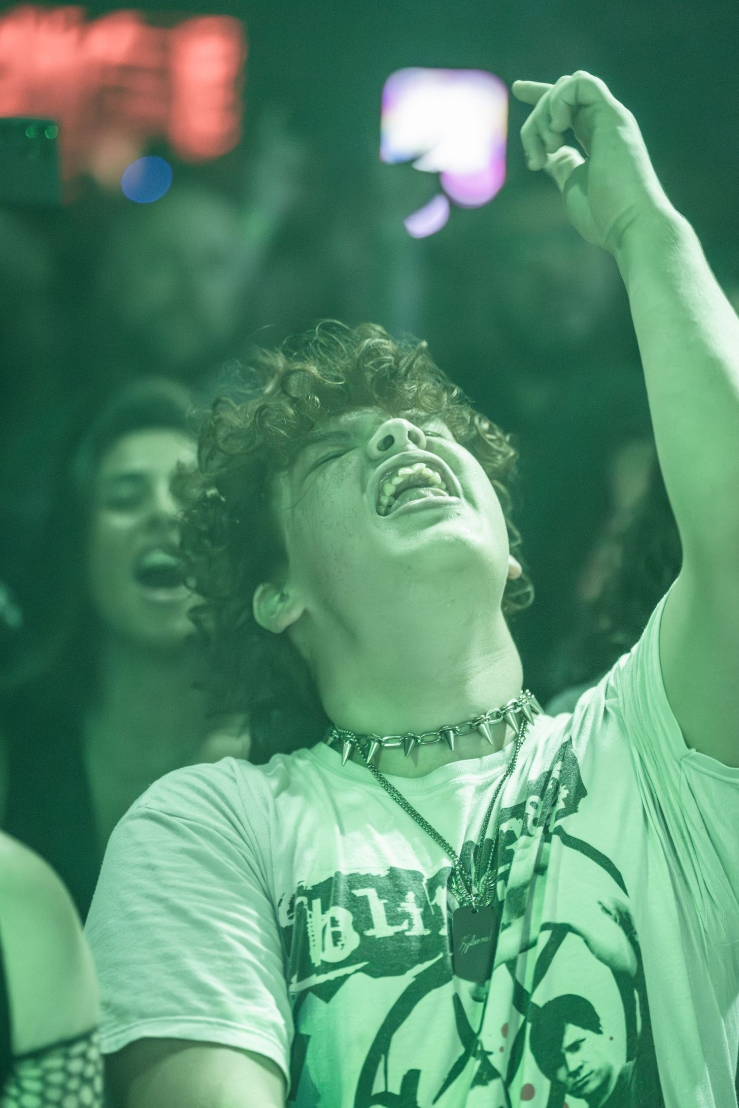 Concert attendee enjoying music with arms raised under green lighting effects.