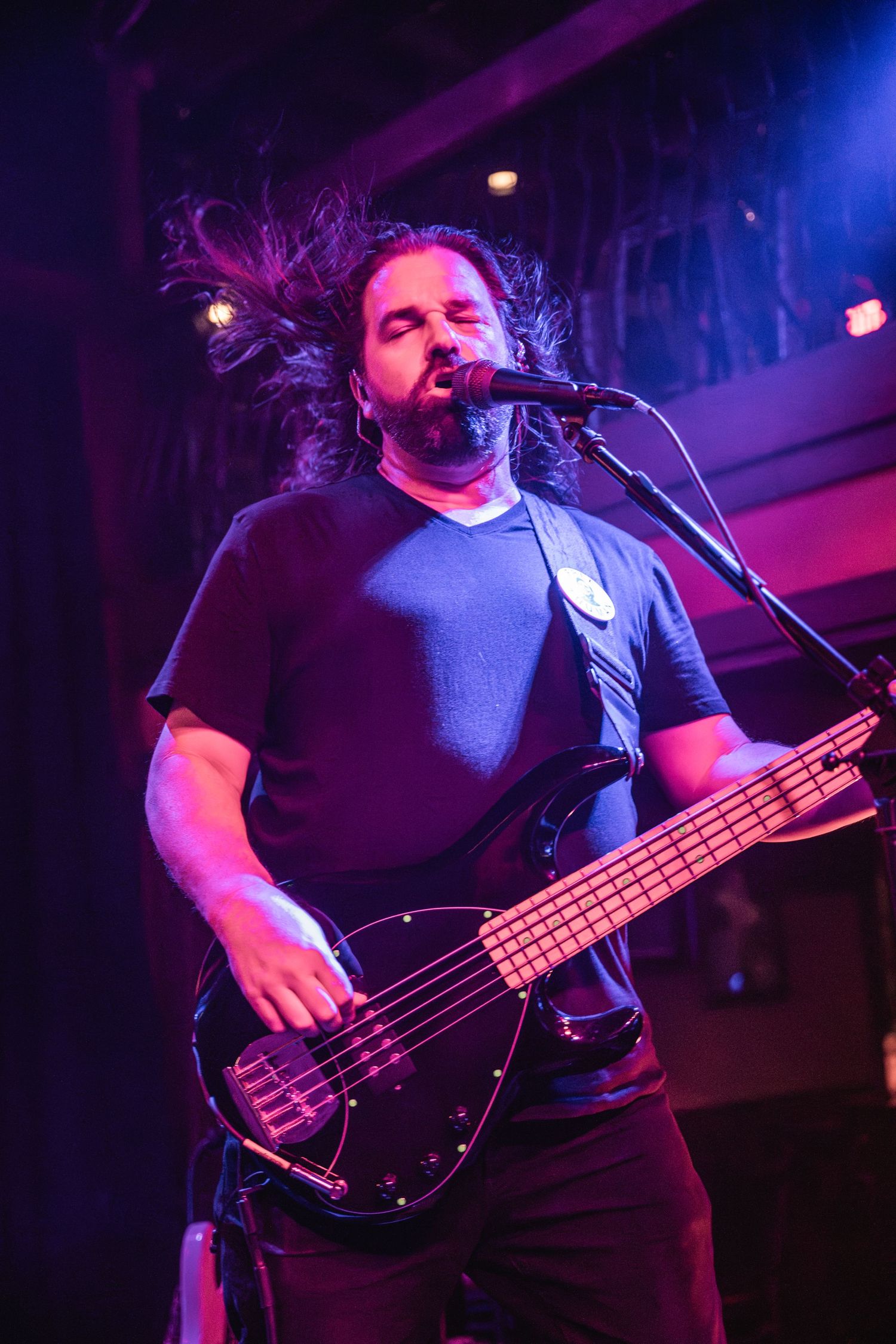 Bass player singing into microphone during live performance with purple stage lighting.