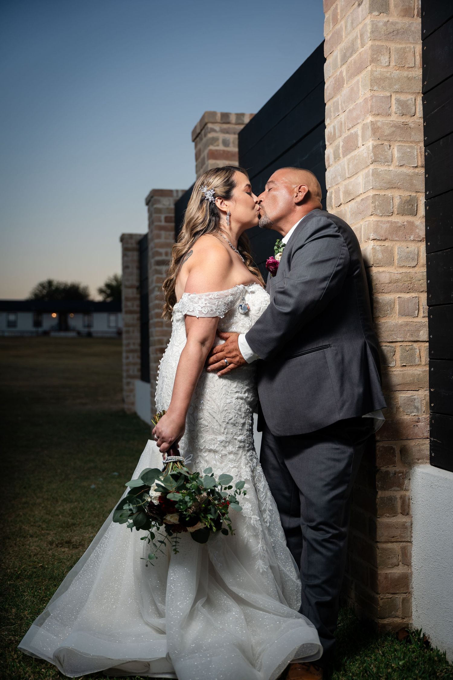 Romantic sunset wedding portrait against brick columns outdoors.