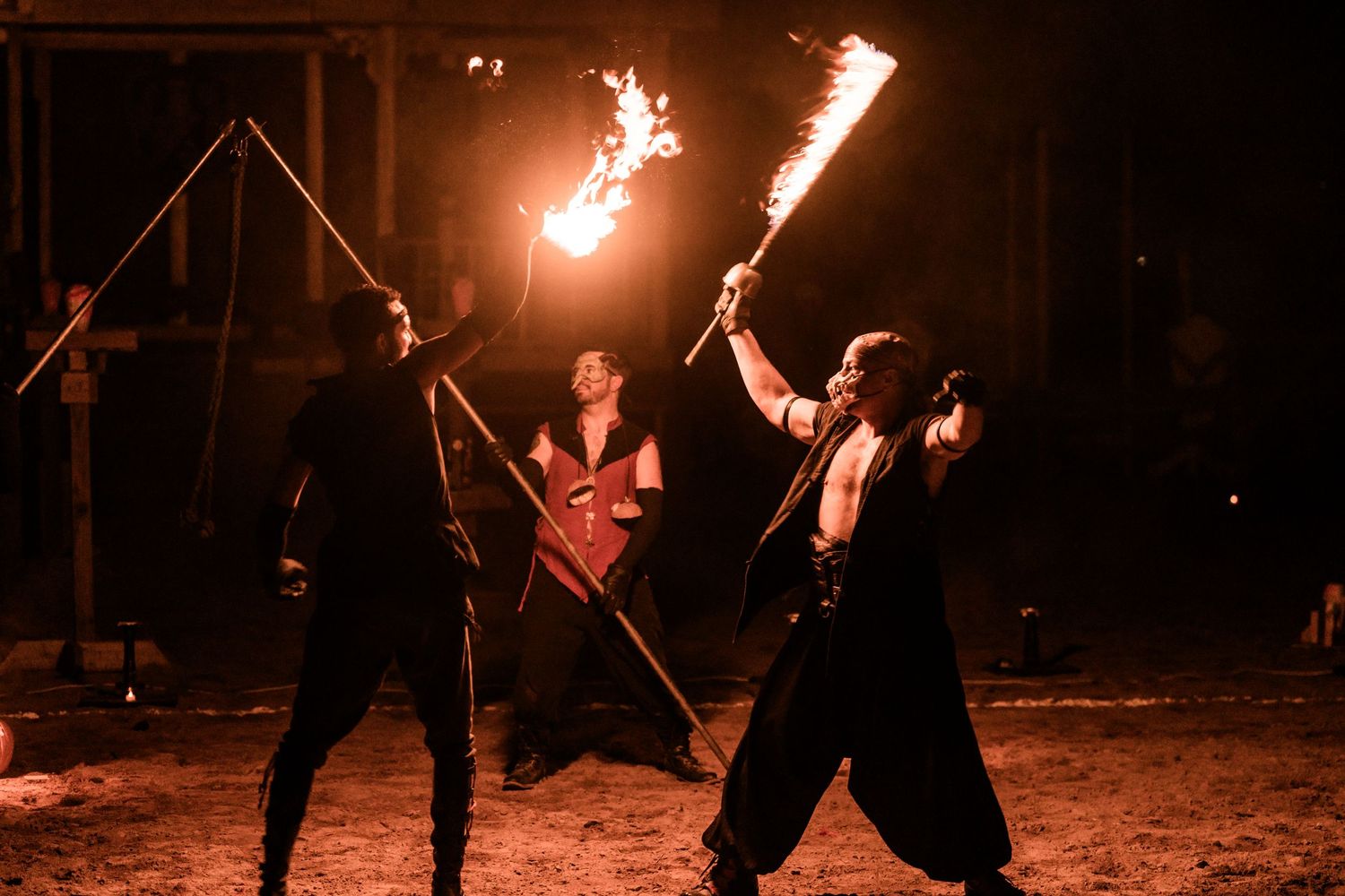 Three performers engage in a choreographed fire staff battle at night.