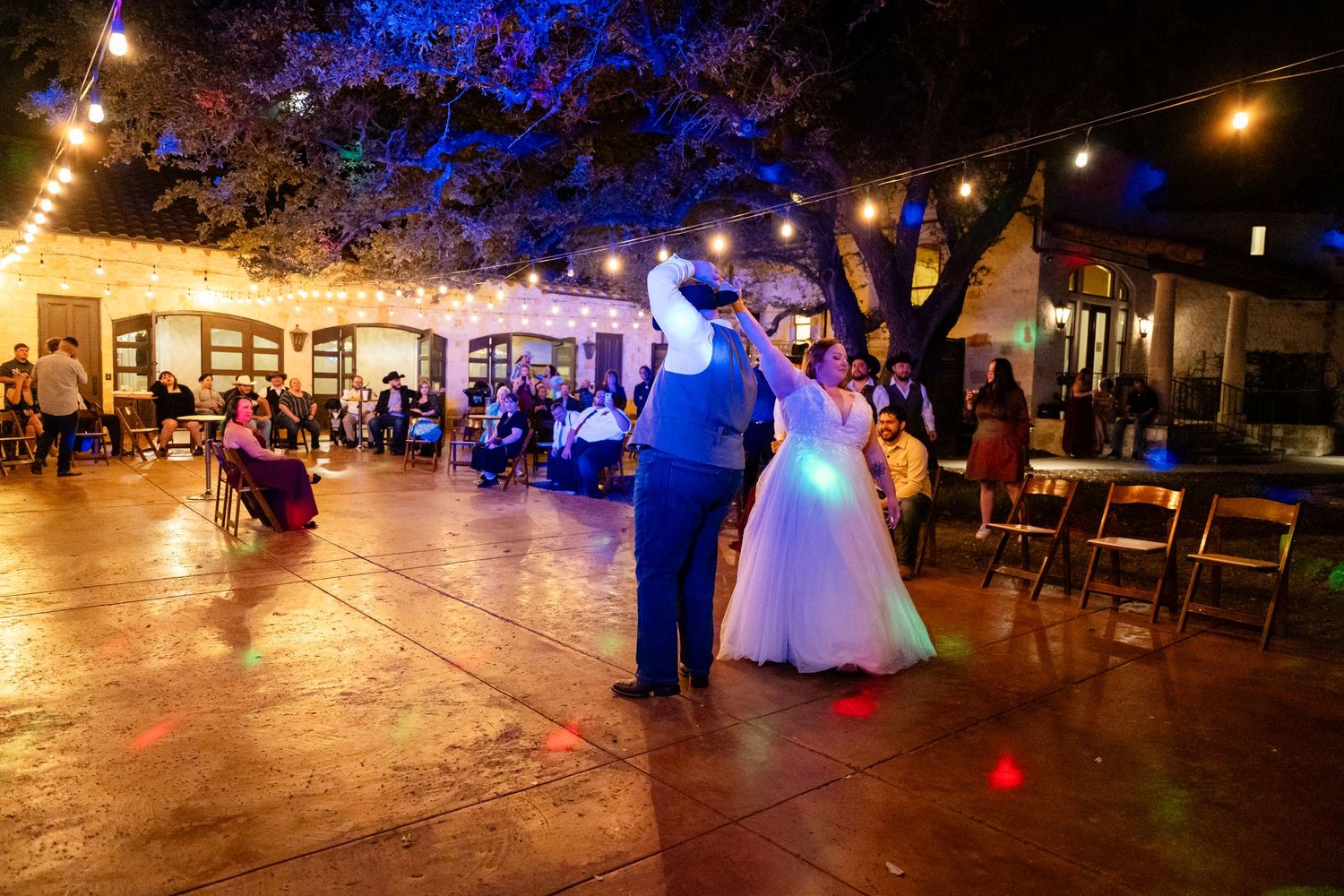 Wedding couple dancing on outdoor patio under string lights and trees.