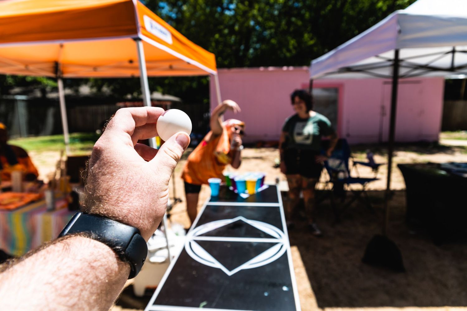 Hands pouring drinks at an outdoor event with tents visible in background.