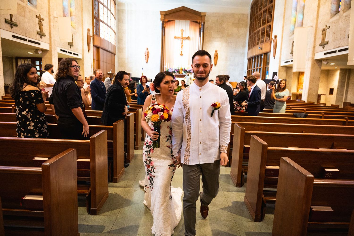 Newlyweds walking down church aisle after ceremony with guests in background.