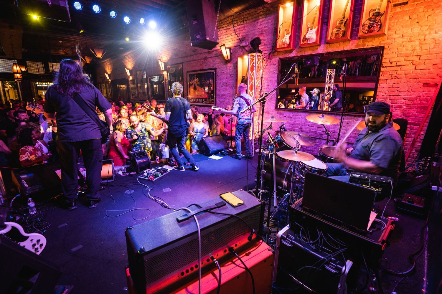 Live music performance in a dimly lit venue with purple and red stage lighting illuminating the brick wall backdrop.