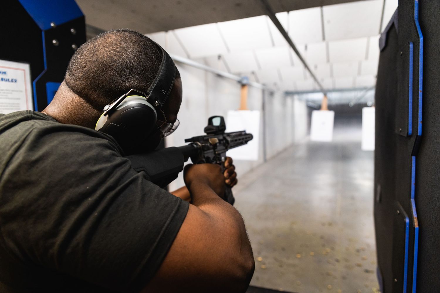 Person in dark shirt aiming firearm down an indoor shooting range lane.