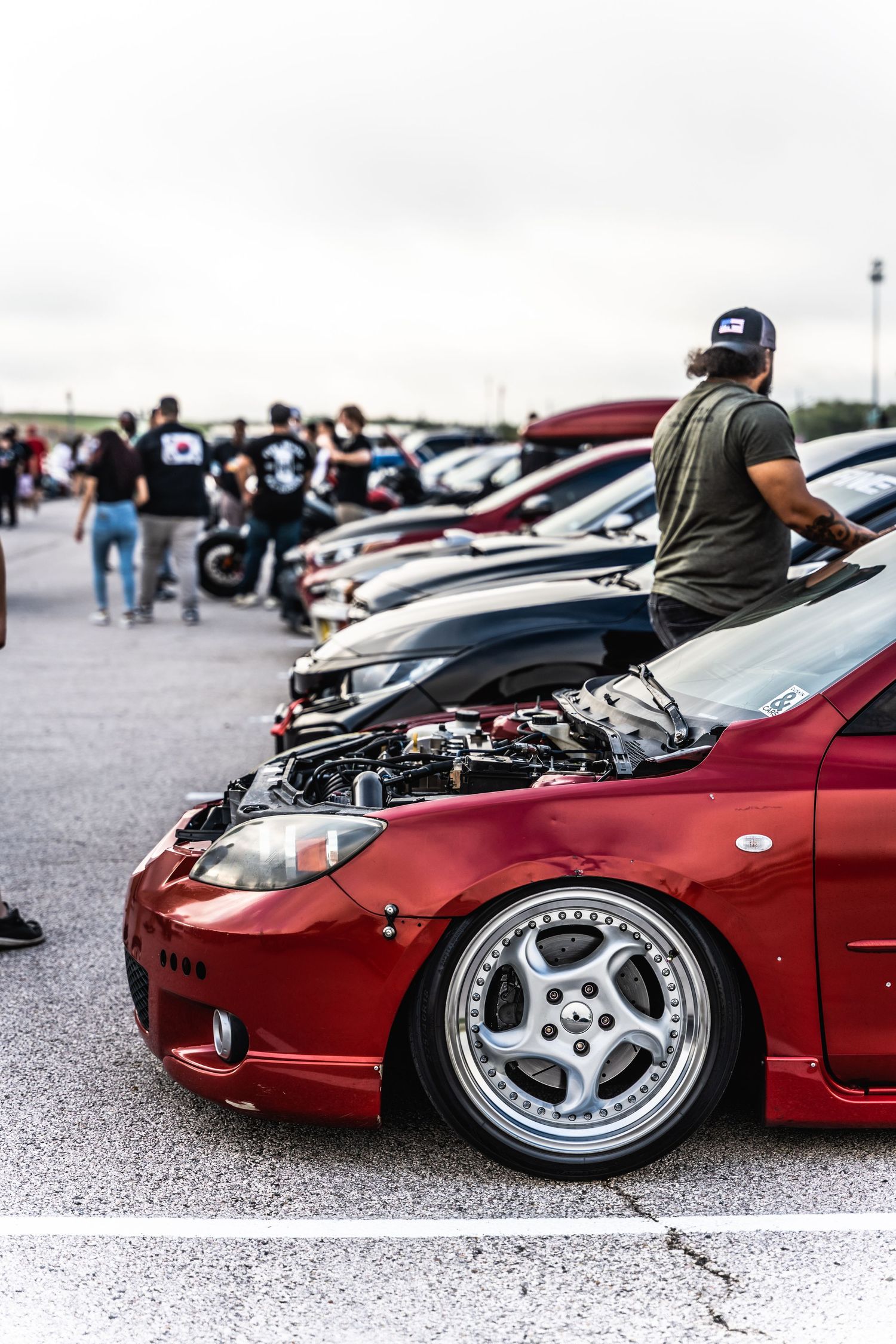 Modified red sports car with custom wheels displayed at an outdoor car meet.