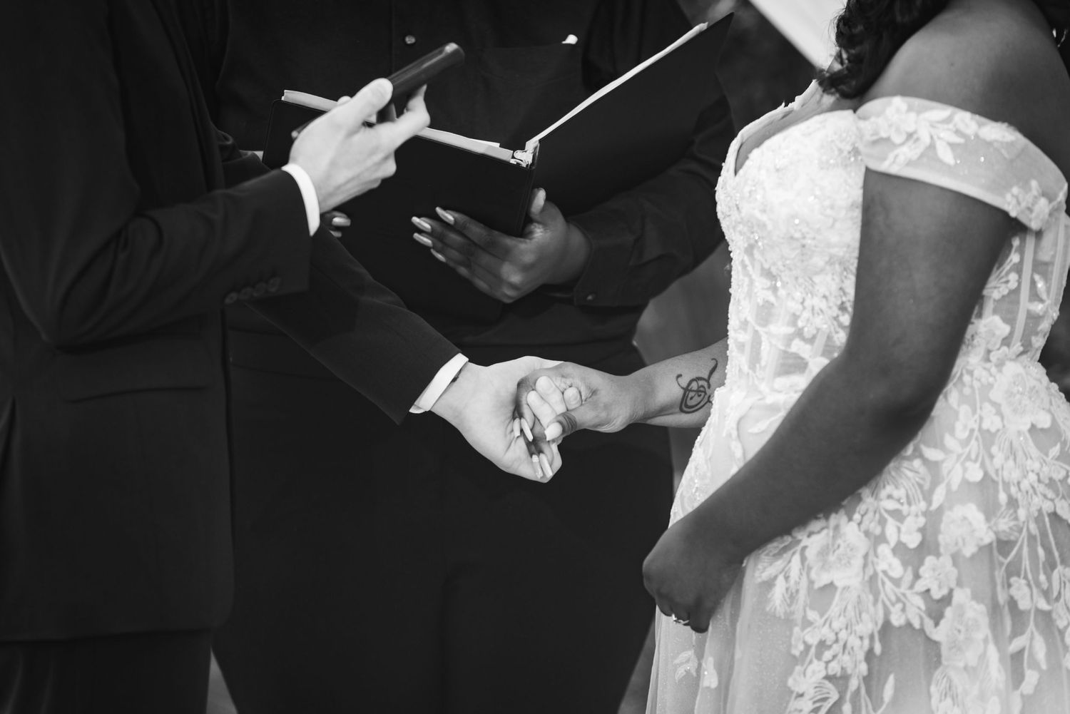 Black and white photo of hands exchanging wedding vows during ceremony.
