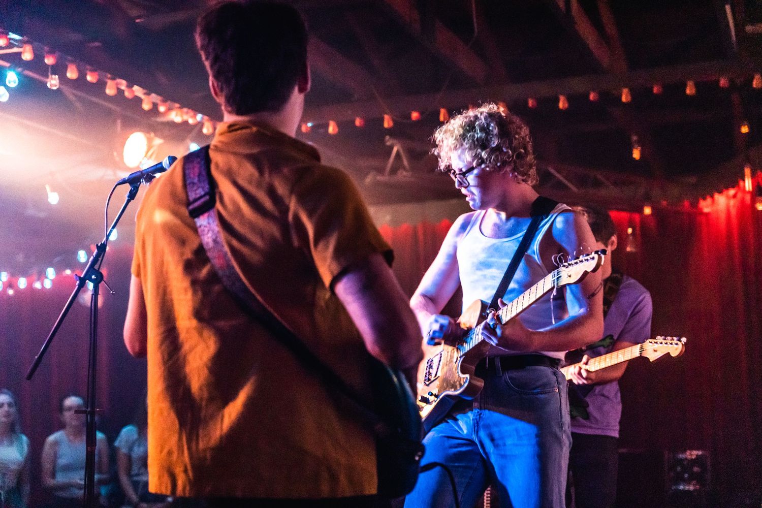 Musicians performing on stage with colorful lighting and guitar at night venue.