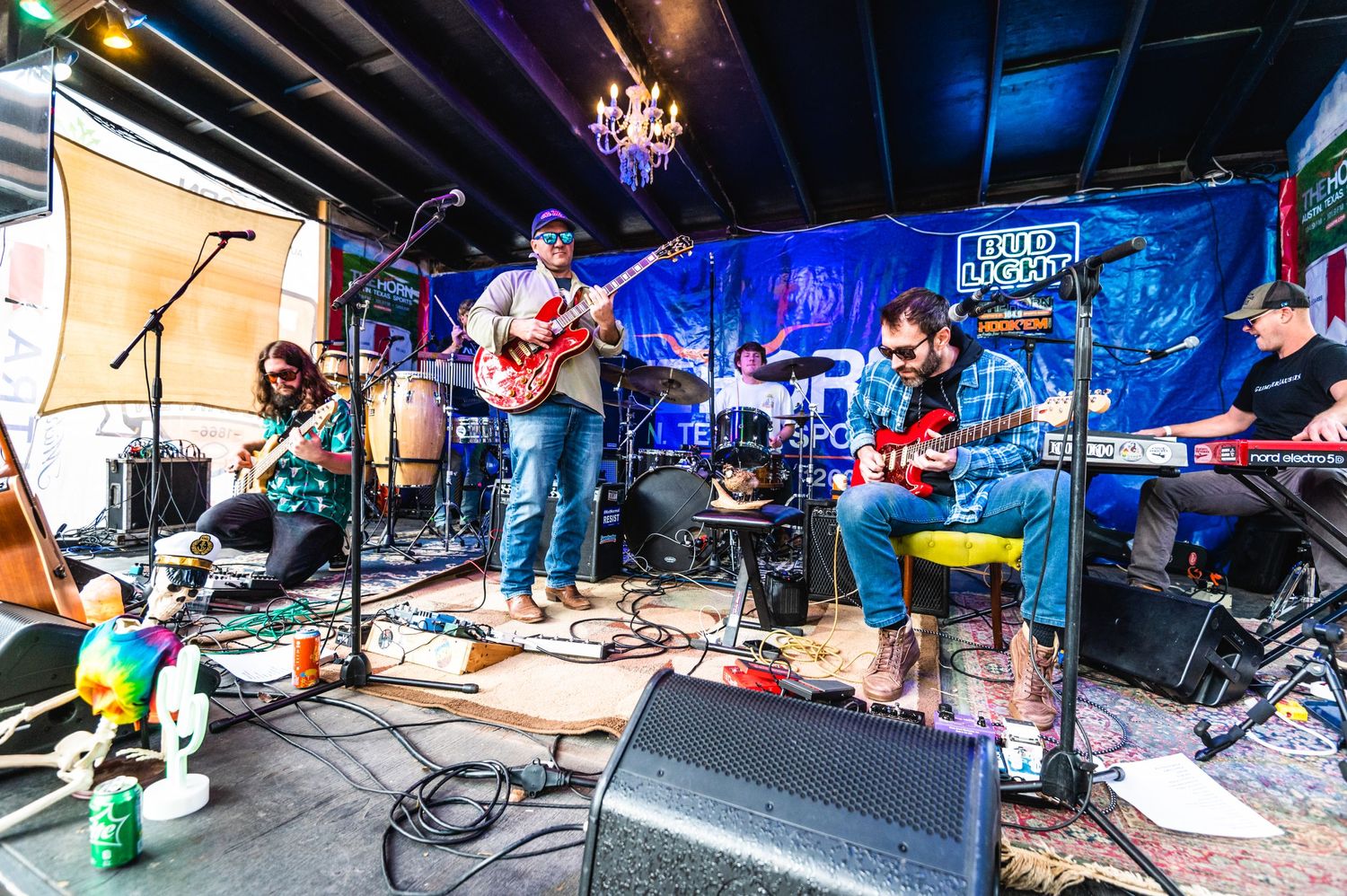 Wide shot of band performing on outdoor stage with blue backdrop and musical equipment.