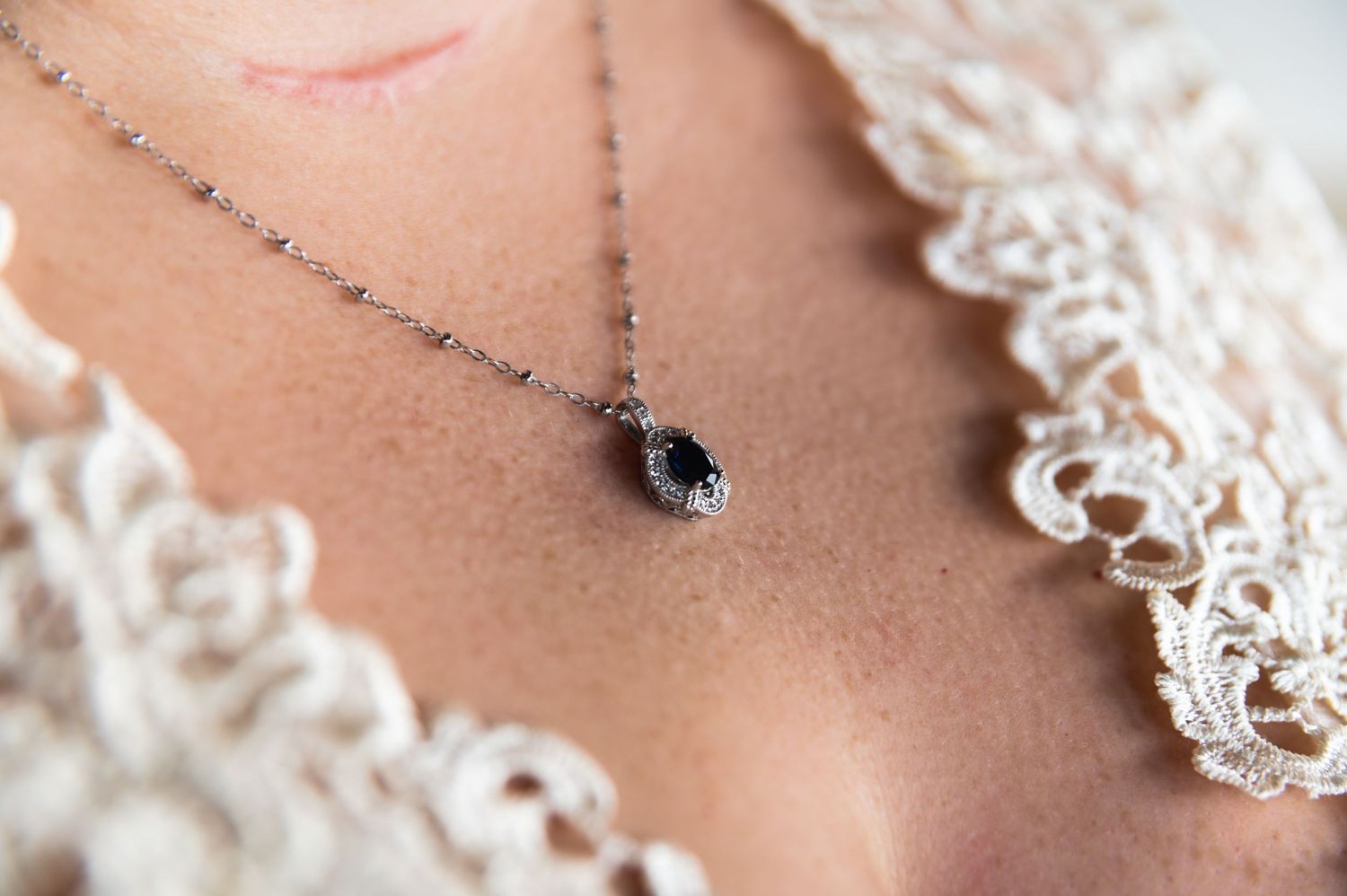 Delicate black crystal pendant necklace against white lace wedding dress.