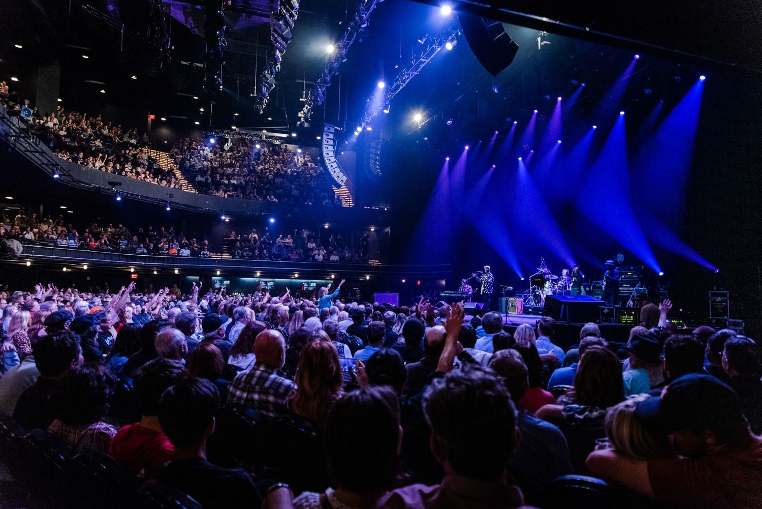 Wide shot of concert venue with blue stage lighting and packed audience visible.
