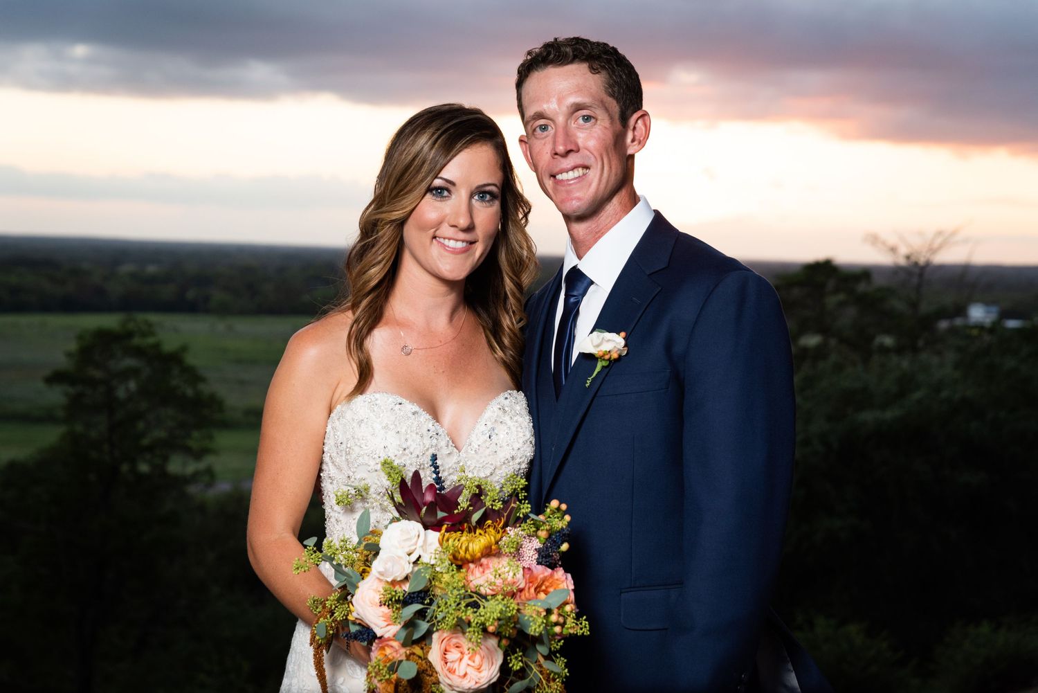 A sunset wedding portrait with colorful bouquet against dramatic evening sky.