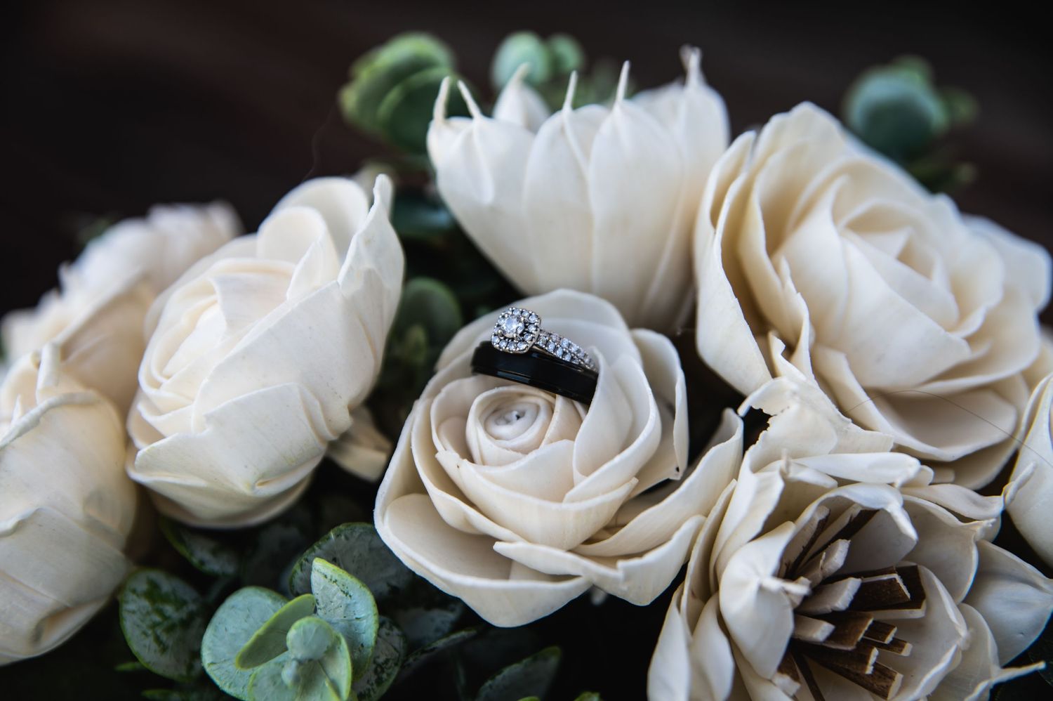 Wedding rings nestled among cream-colored artificial roses in a bridal bouquet.
