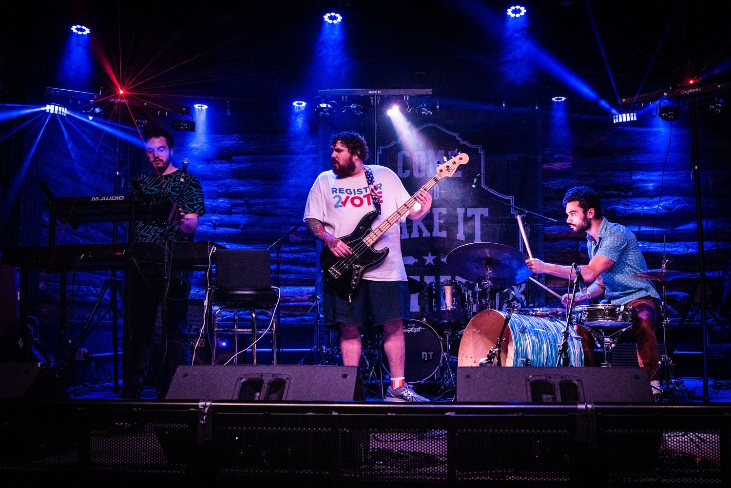 Band performing on stage with blue spotlights and drum kit visible in concert setting.