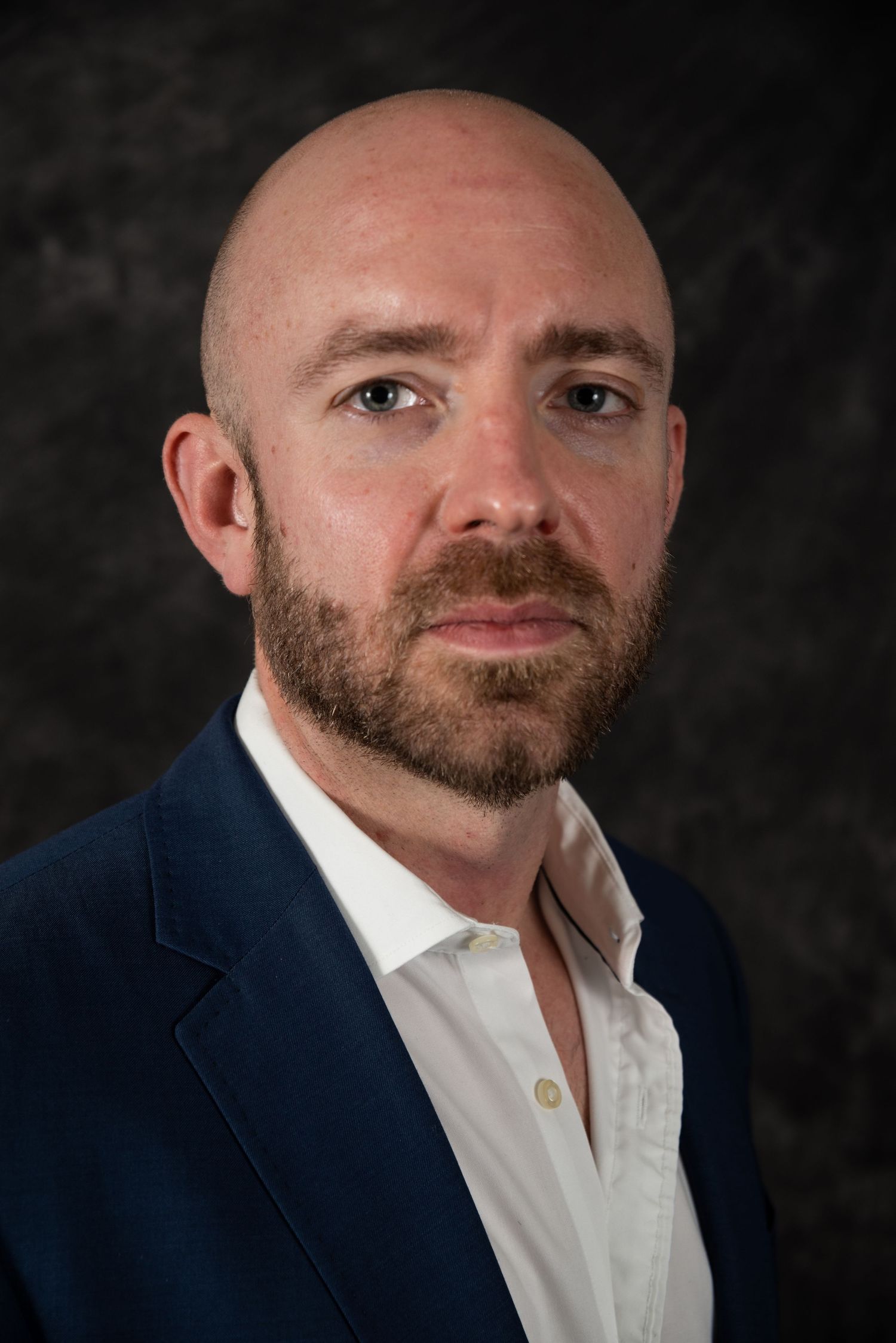 Professional studio portrait showing person in business attire against textured dark background.