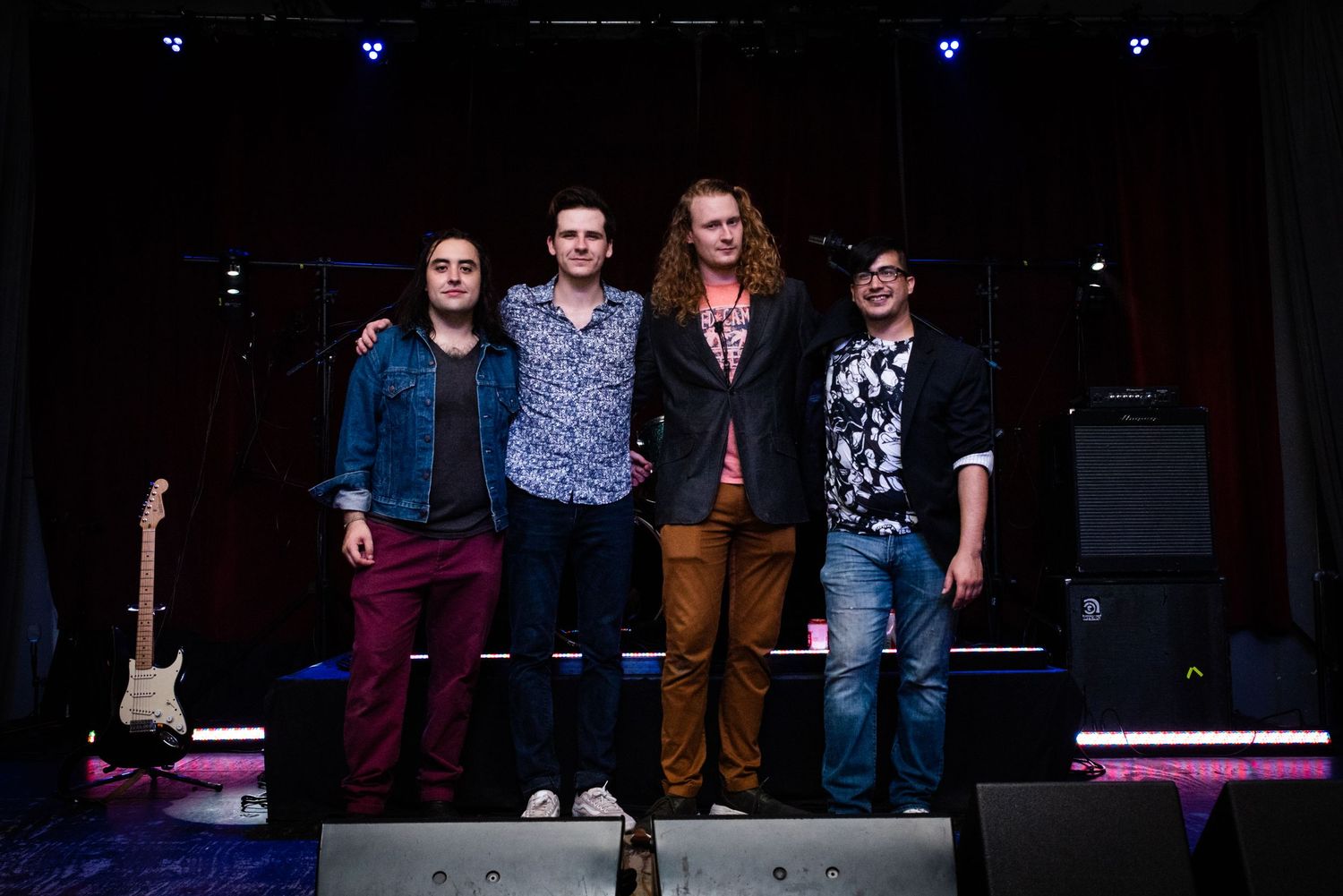 Band members stand together on stage for a group photo with instruments and equipment.