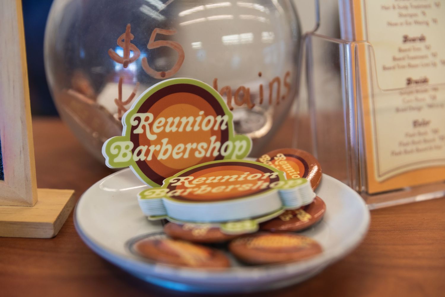 Close-up of Reunion Barbershop logo on glass with blurred dessert plate in foreground.