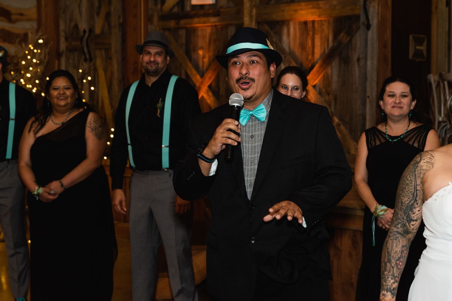A wedding reception speaker entertains guests inside a rustic barn venue.