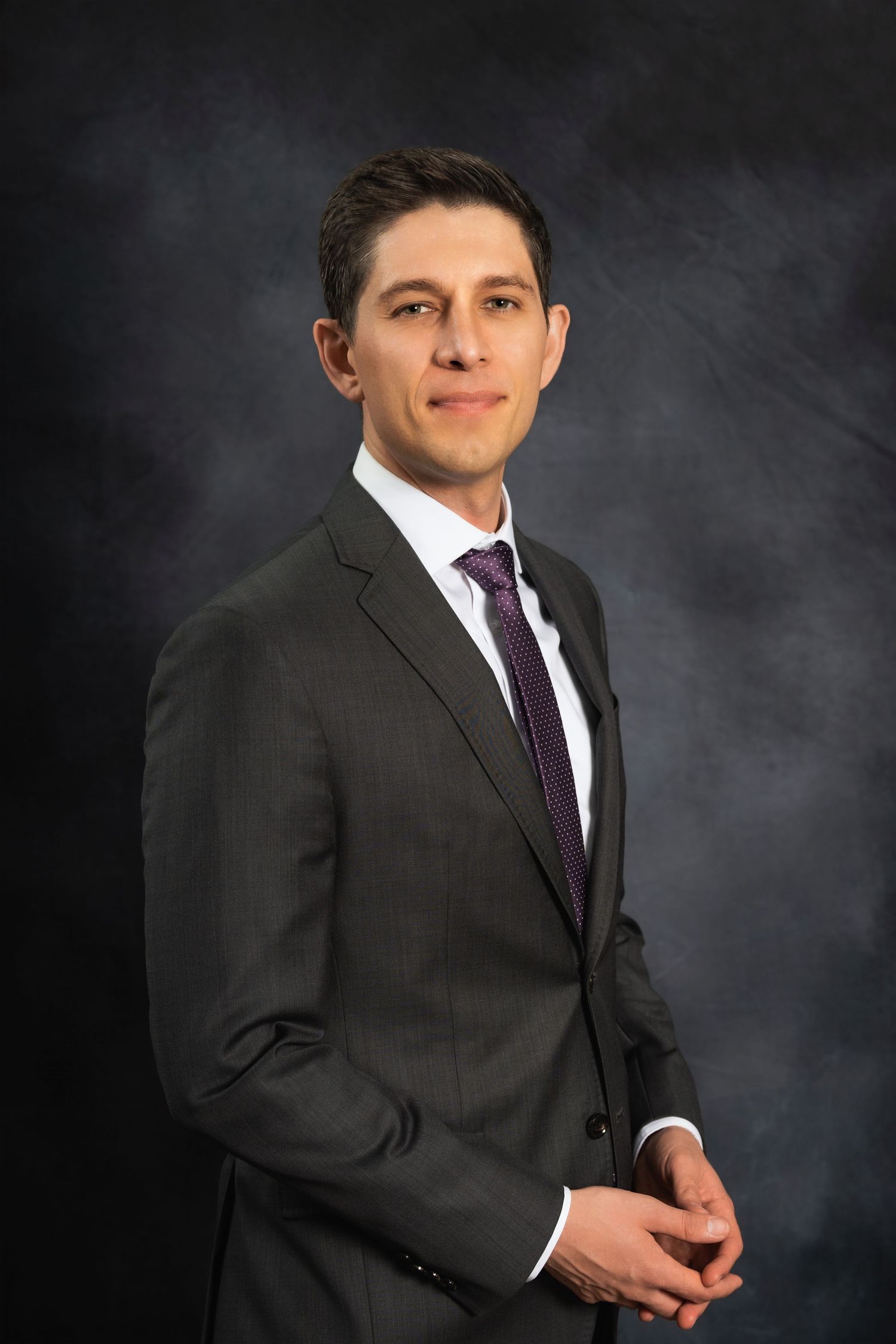 Business portrait showing a professional in dark suit and purple tie against gray backdrop.