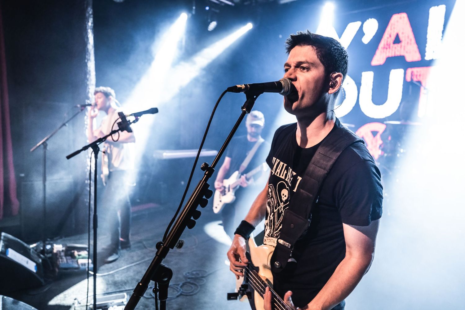 Musician singing and playing guitar in front of Y'all Out Boy backdrop during live performance.