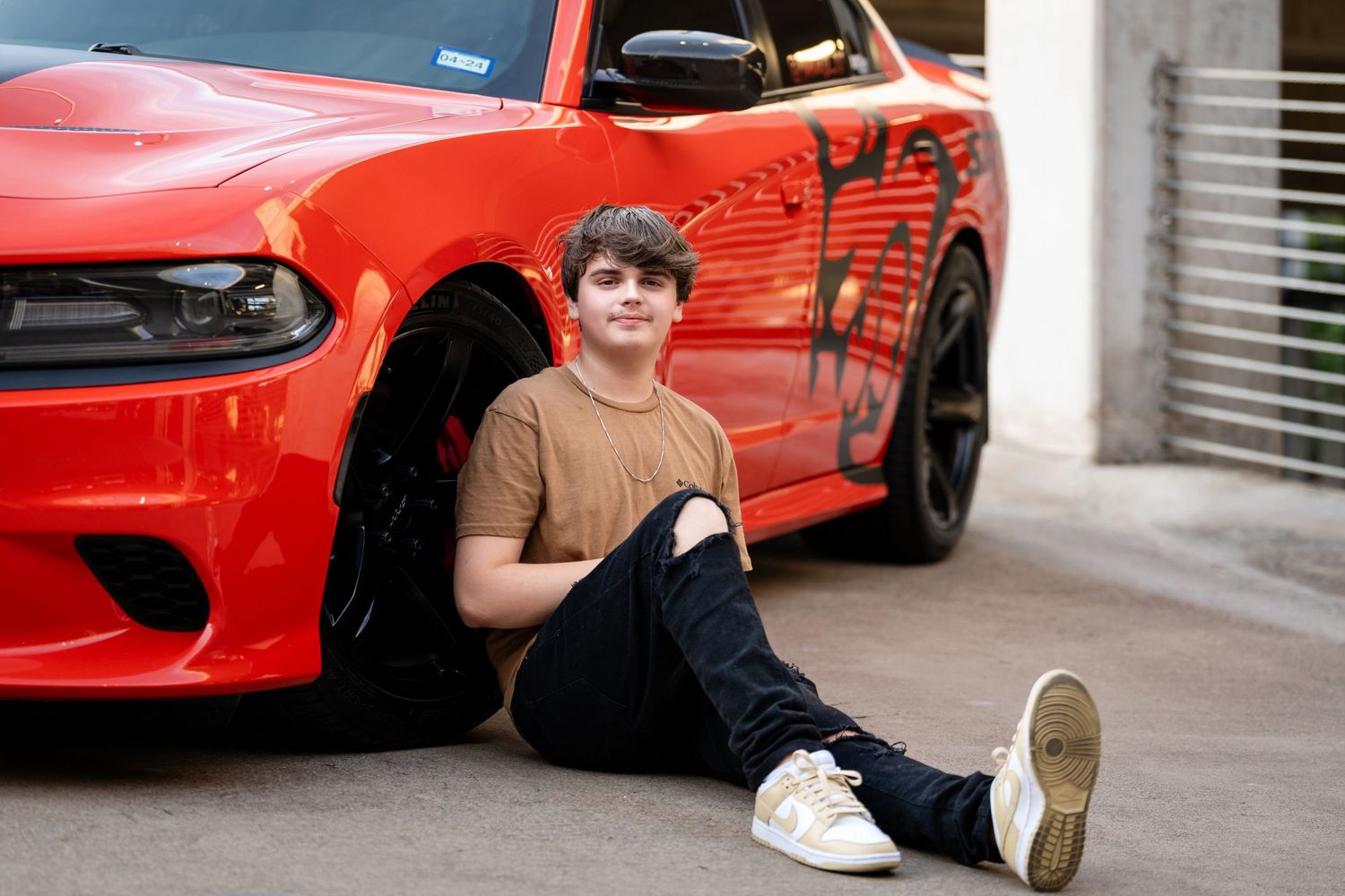 A relaxed portrait beside a customized red Dodge Charger in a concrete parking structure.
