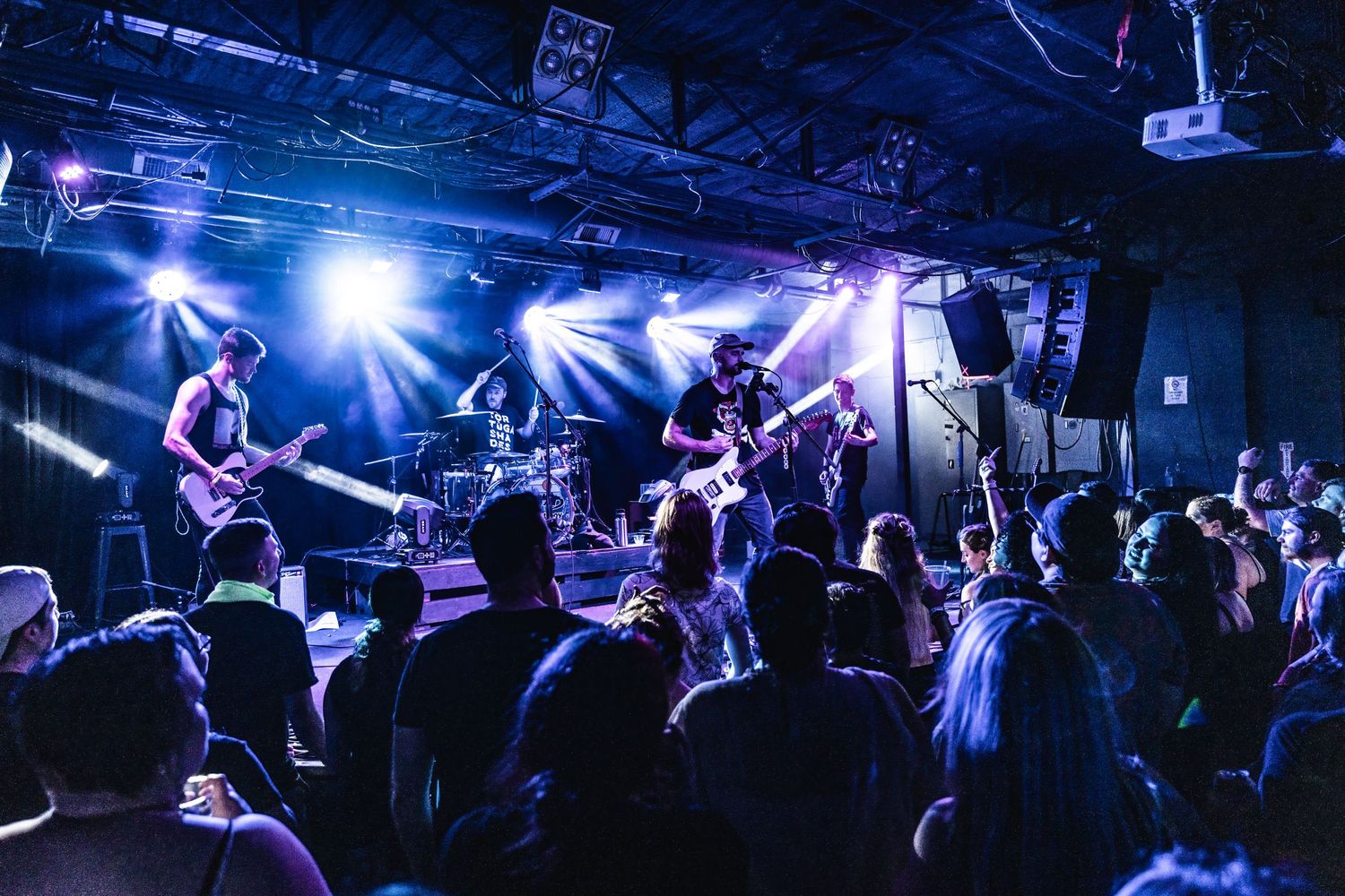 Rock band performs on stage with dramatic blue backlighting as crowd watches.