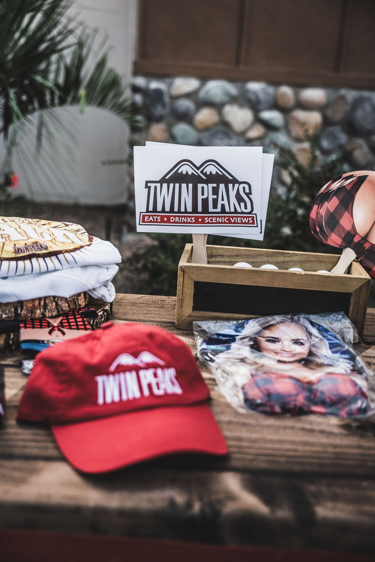 Twin Peaks logo display with branded merchandise and baseball caps arranged on wooden table.