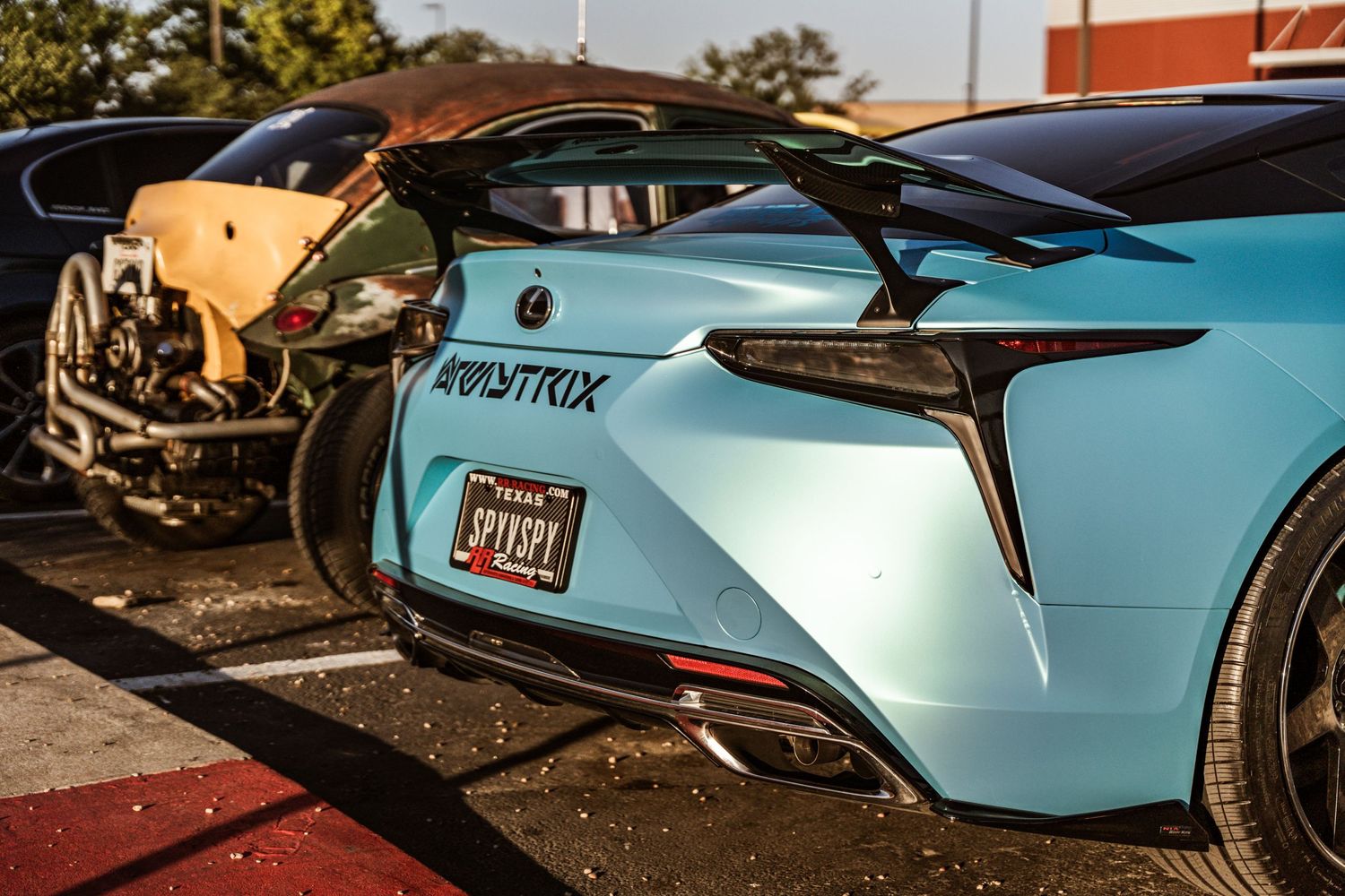 Light blue Lexus sports car with custom spoiler parked in lot.