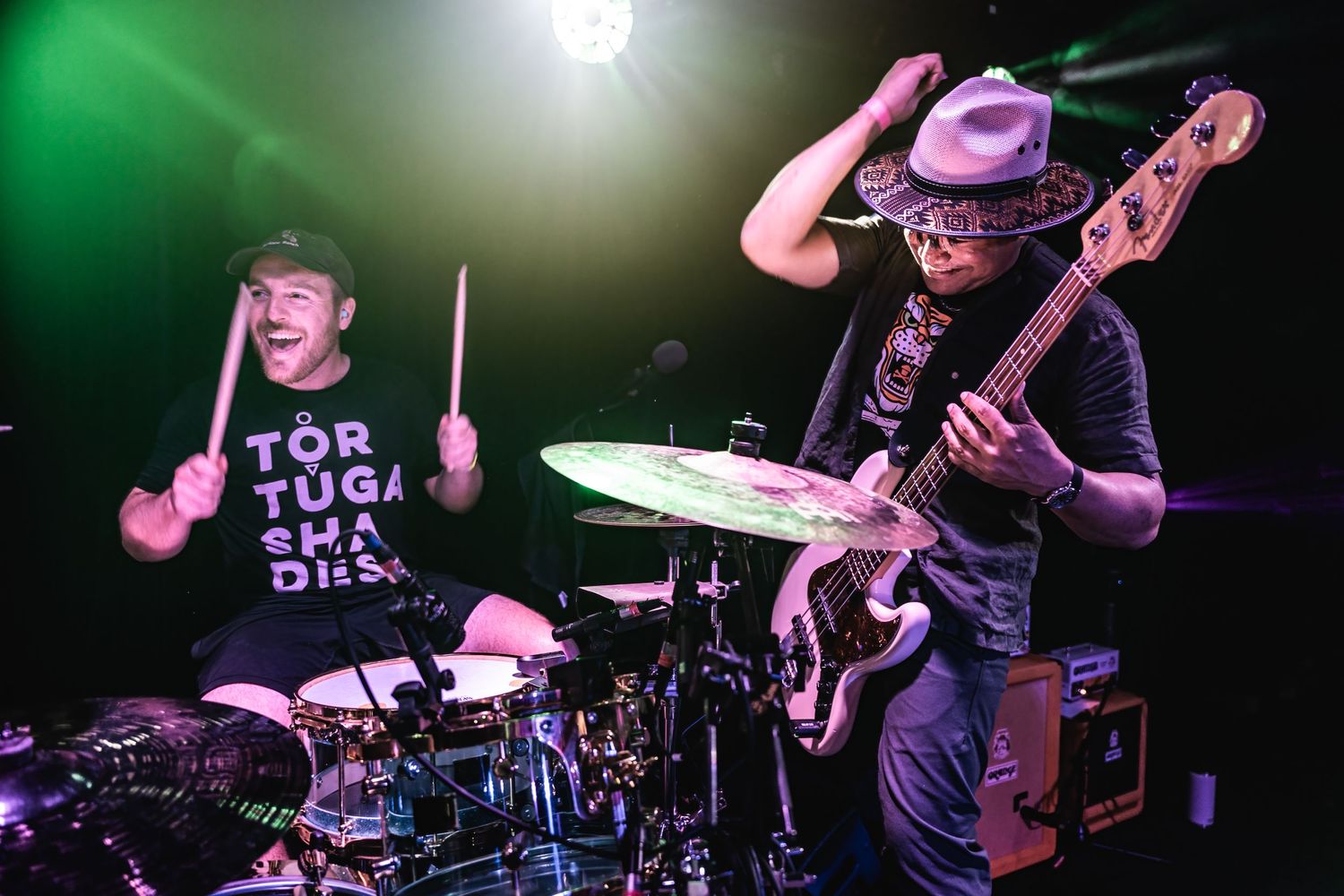 Drummer and bassist perform together under bright green stage lighting during live show.