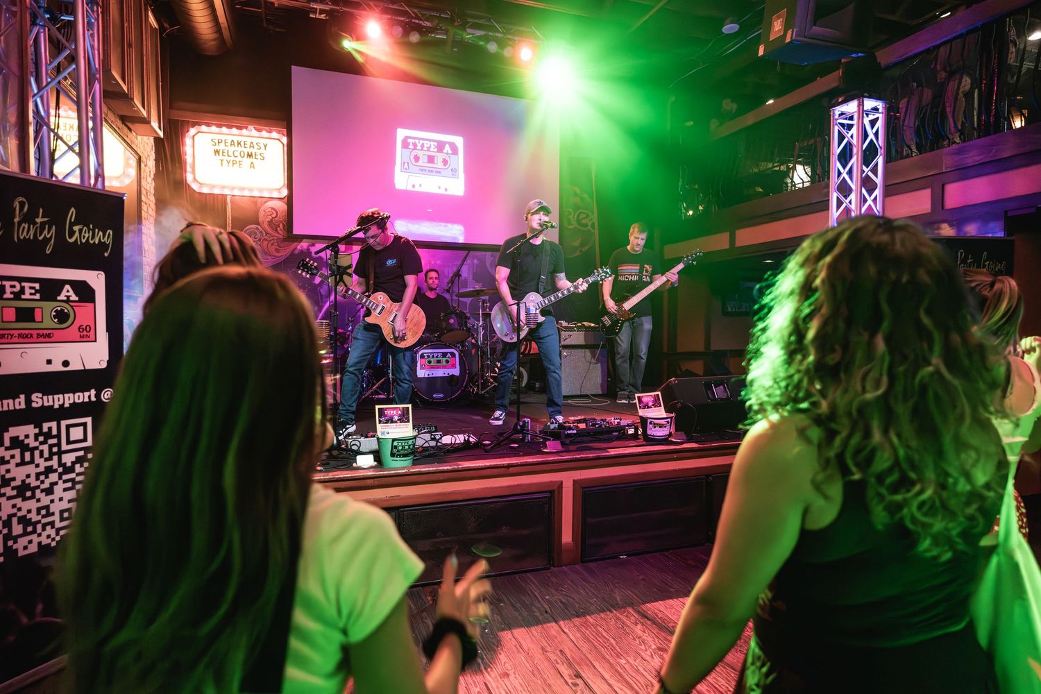 View from audience showing band performing on elevated stage with pink and green lighting.
