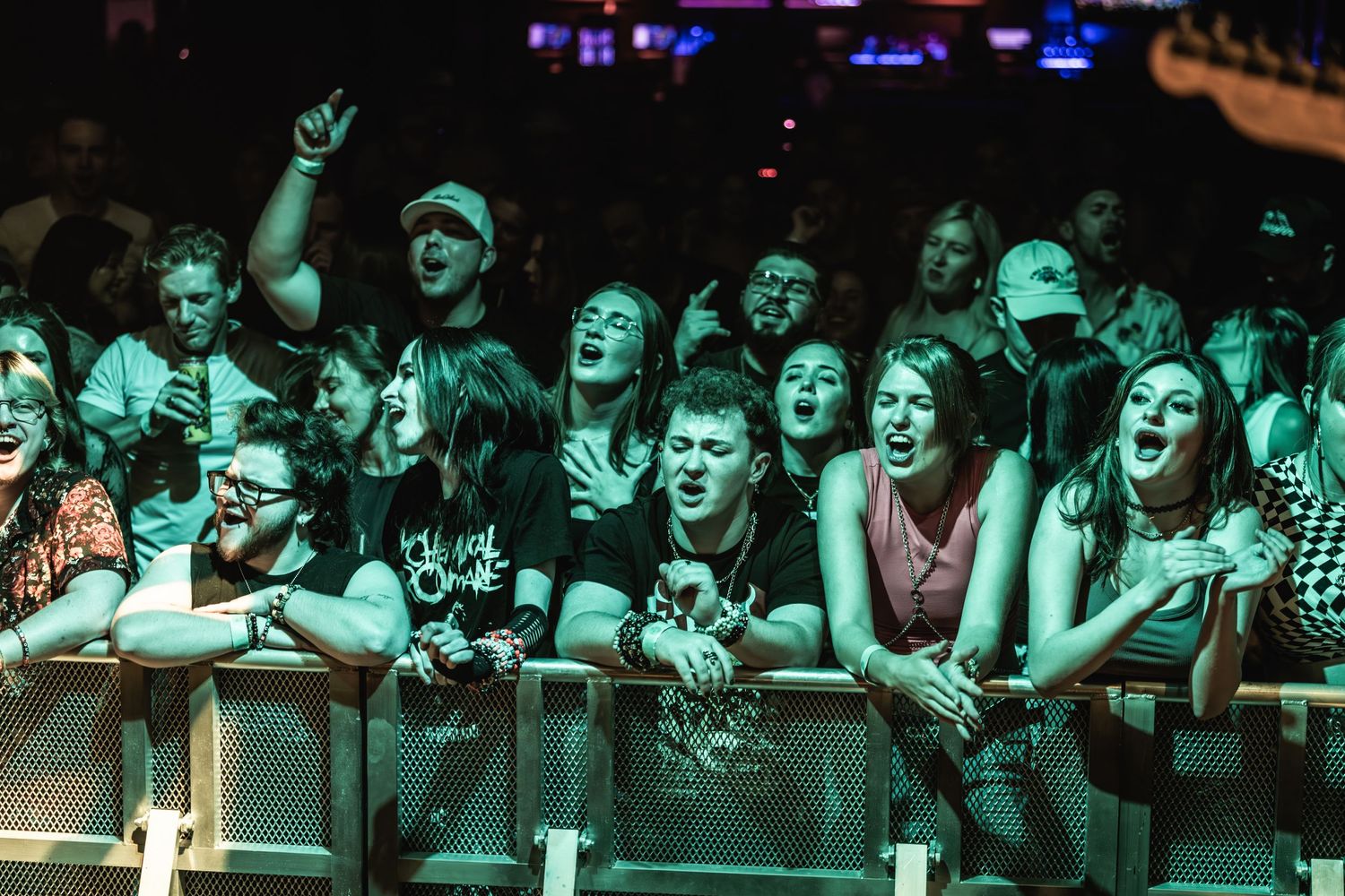 Enthusiastic fans packed against the front barrier at rock concert with teal lighting.