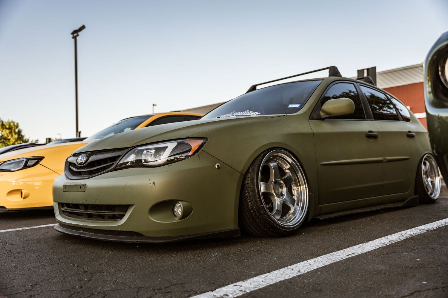 A lowered olive green Subaru WRX with custom wheels parked in a parking lot.