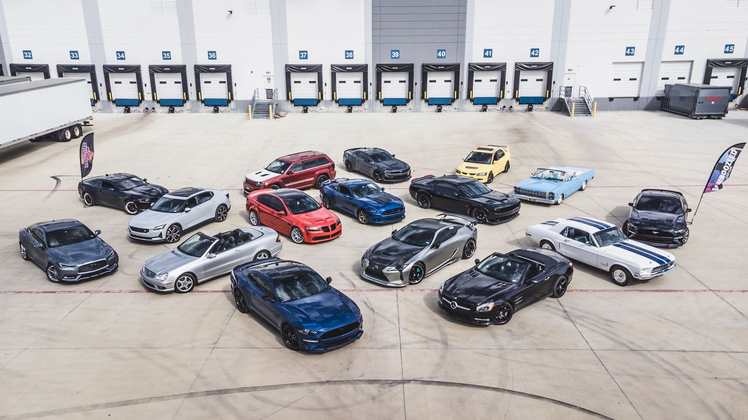 Diverse group of performance vehicles displayed in formation at an industrial loading dock.