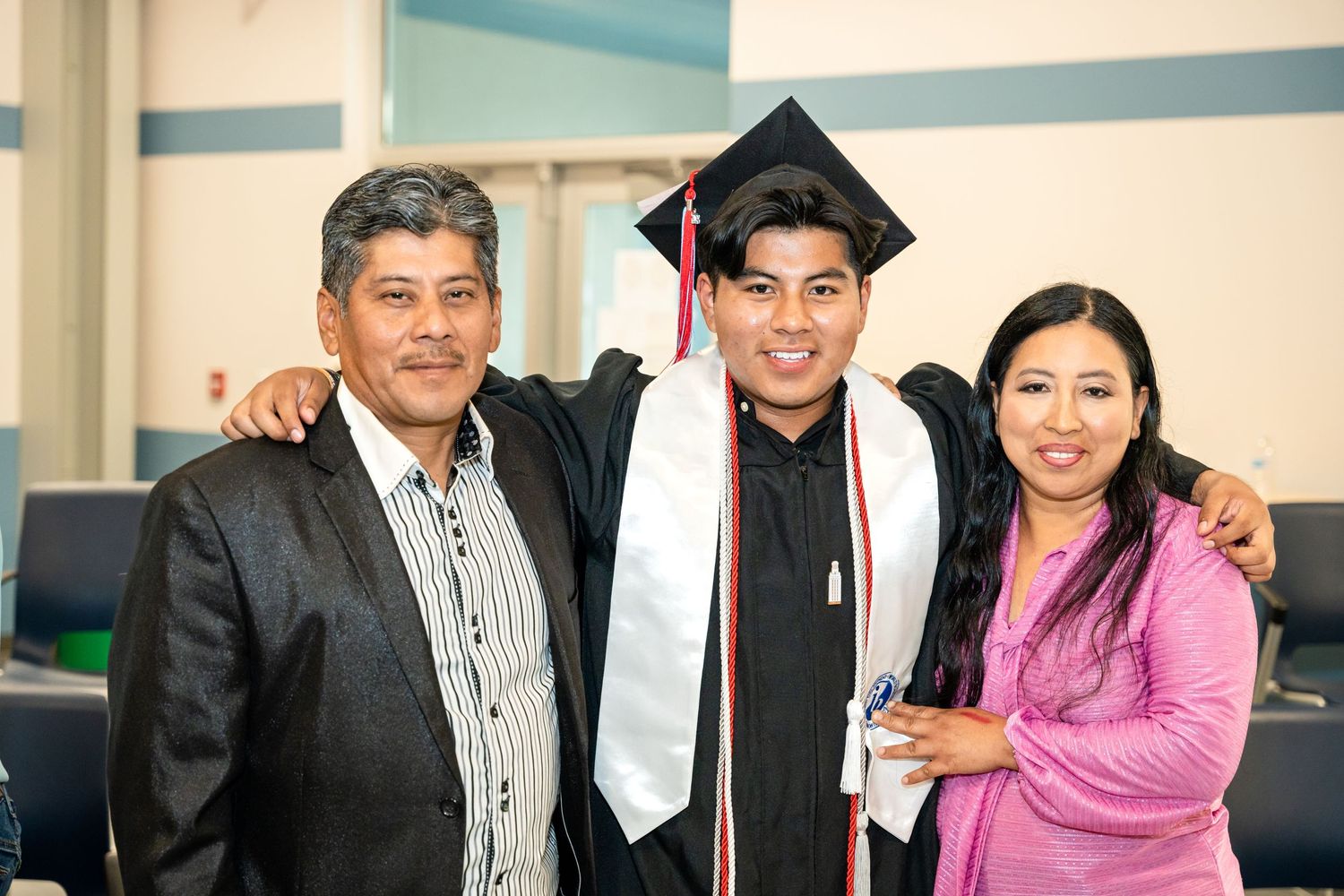 Graduate in cap and gown poses with family members at graduation celebration.