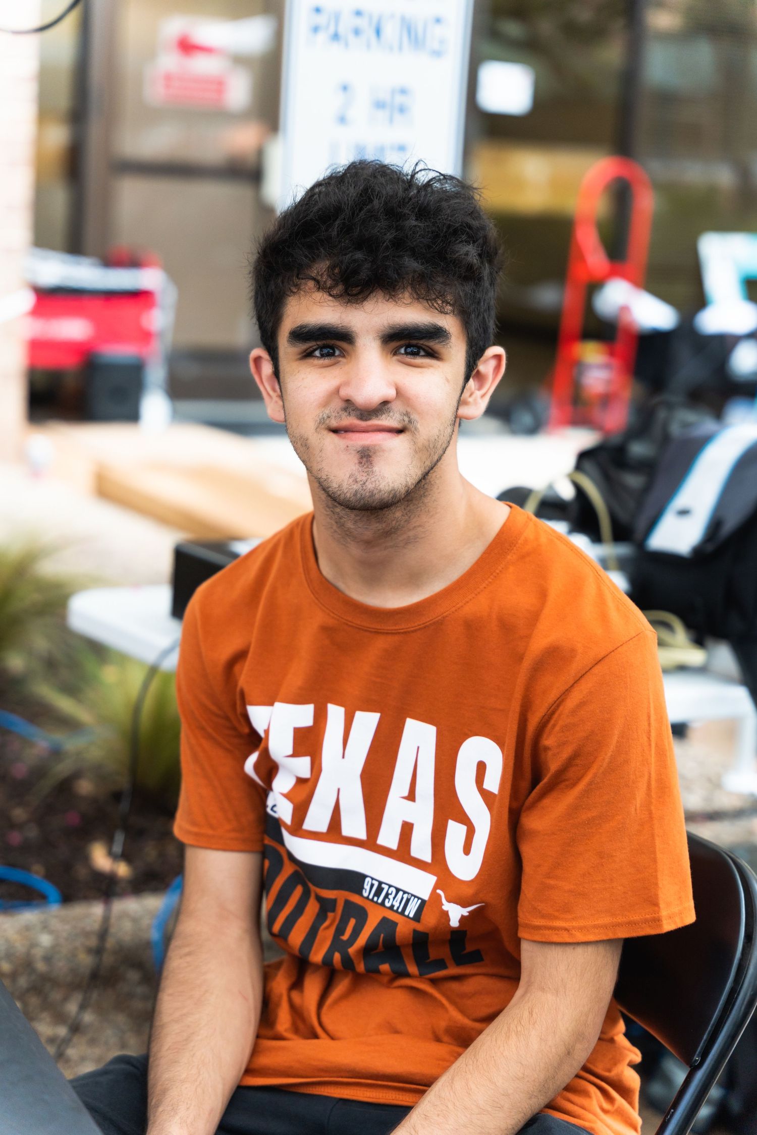 Student wearing a burnt orange Texas football shirt sits outdoors on campus.