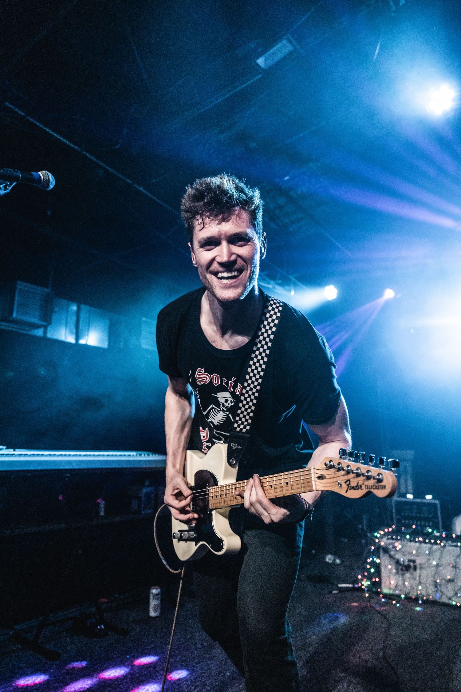 Guitarist performing energetically on stage under blue concert lighting.
