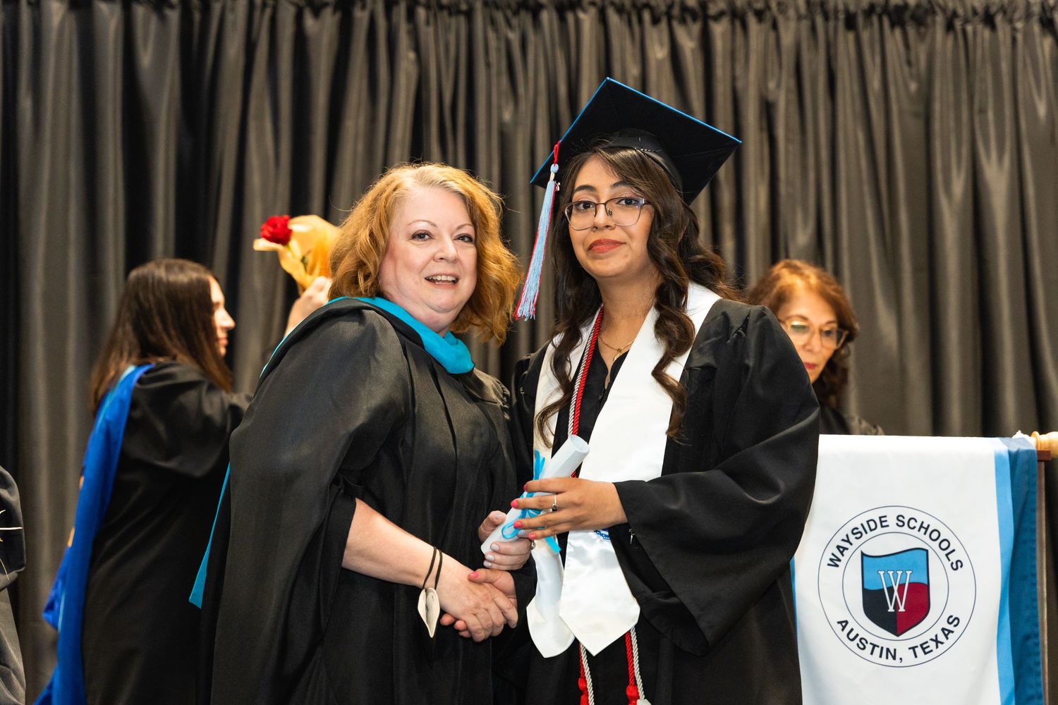 Two graduates in academic regalia sharing a celebratory moment at commencement ceremony.