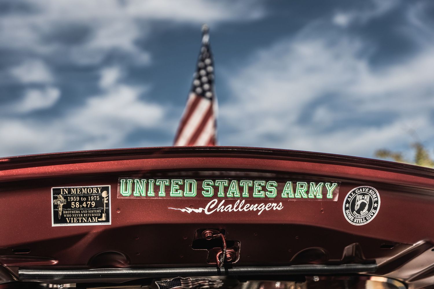 Close-up of United States Army Challenger decal on red vehicle against blue sky with American flag.