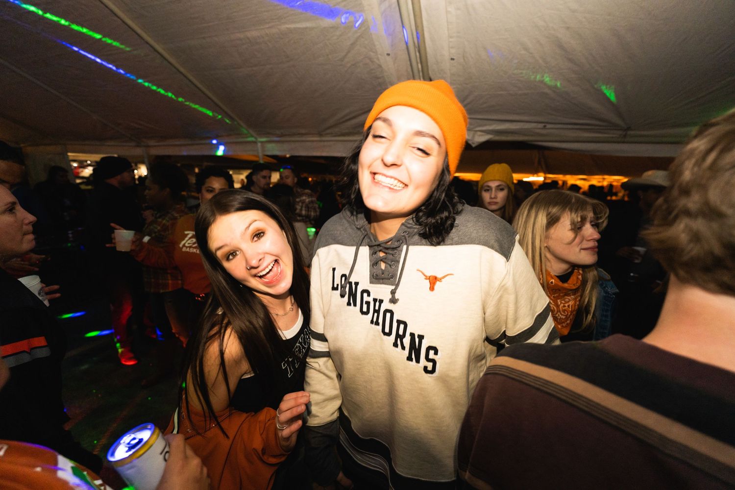 Party scene with colorful laser lights and people celebrating under a tent structure.