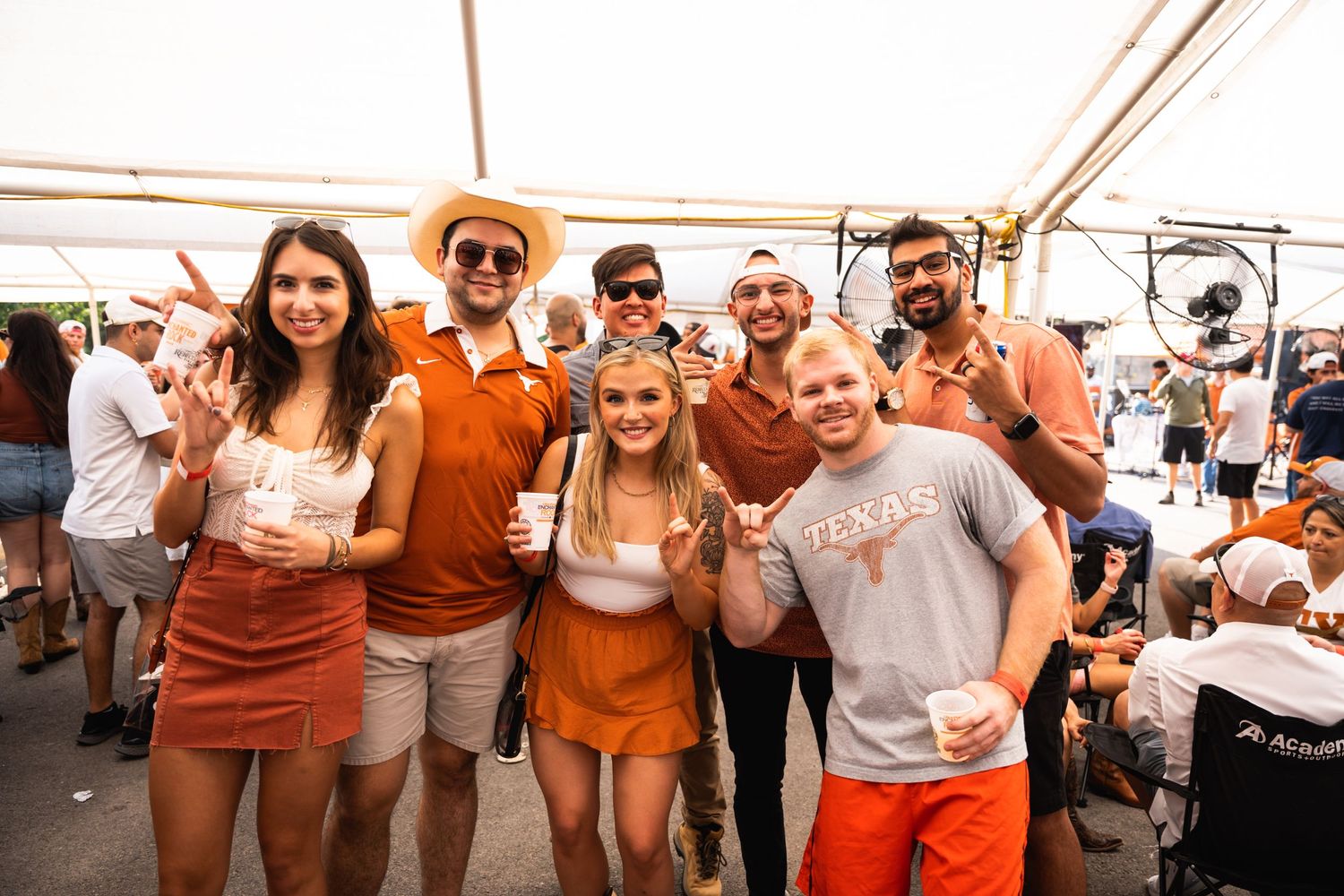 Group wearing orange and white attire poses together at outdoor celebration.