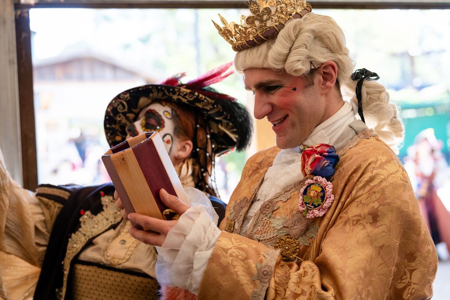 A group of people in period costumes and wigs sit at a table during a historical reenactment event.